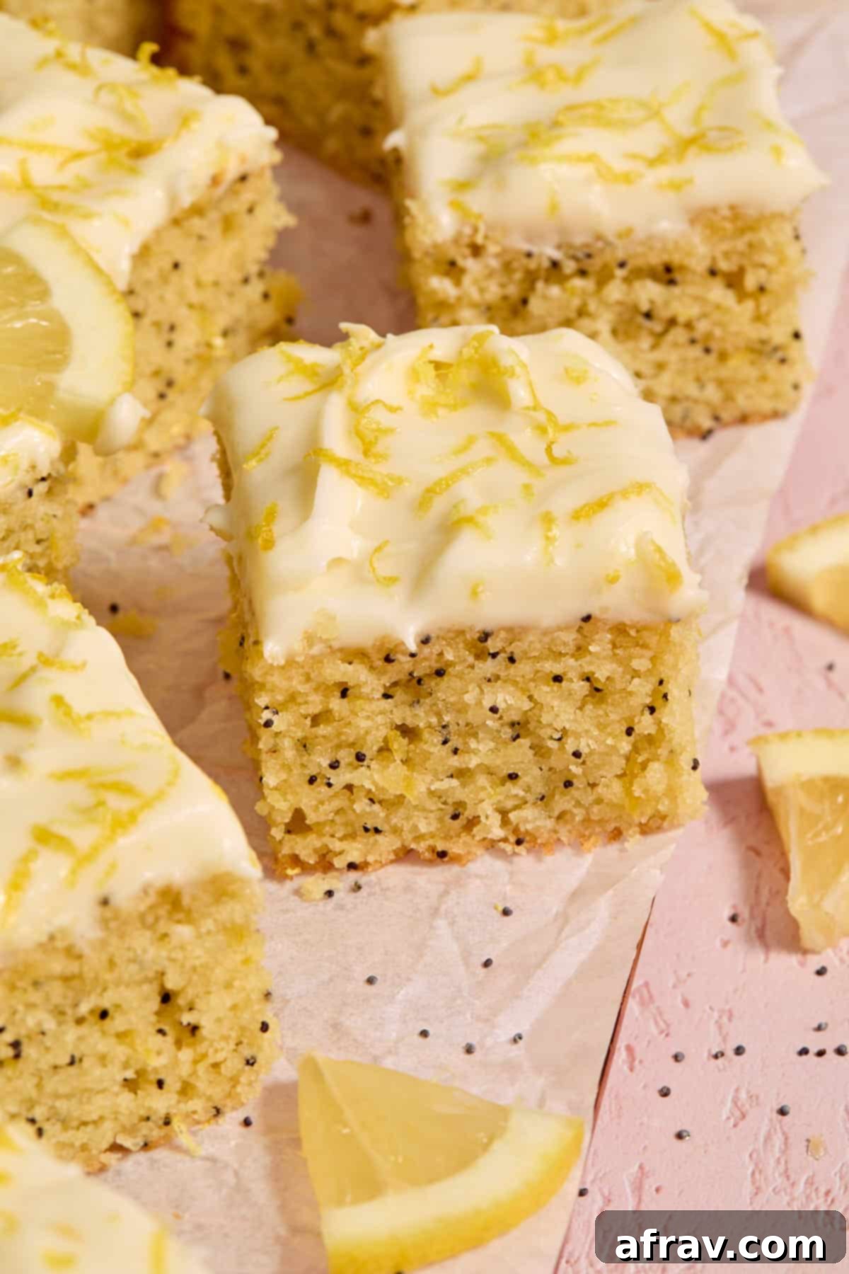 Pieces of gluten-free almond flour lemon poppy seed cake on parchment paper with poppy seeds and fresh lemon slices scattered around.