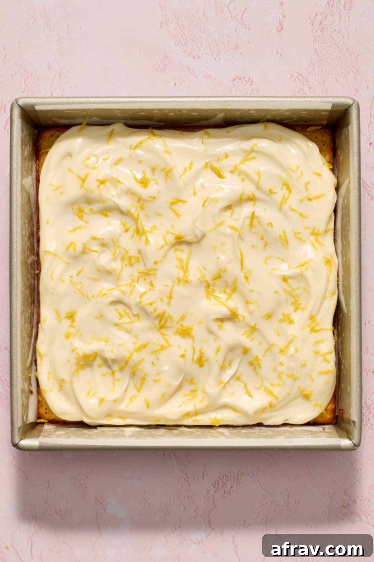 Finished almond flour lemon poppy seed cake with smooth cream cheese frosting spread over it, garnished with fresh lemon zest.