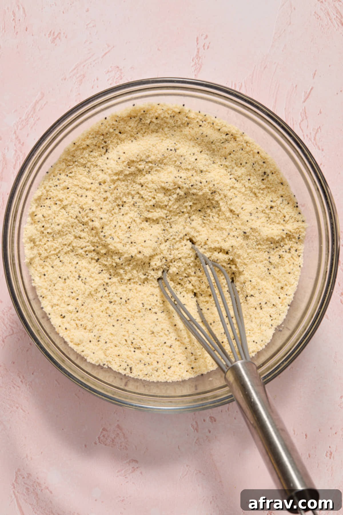 Dry ingredients for the cake, including poppy seeds, baking powder, and almond flour, whisked together in a glass bowl.