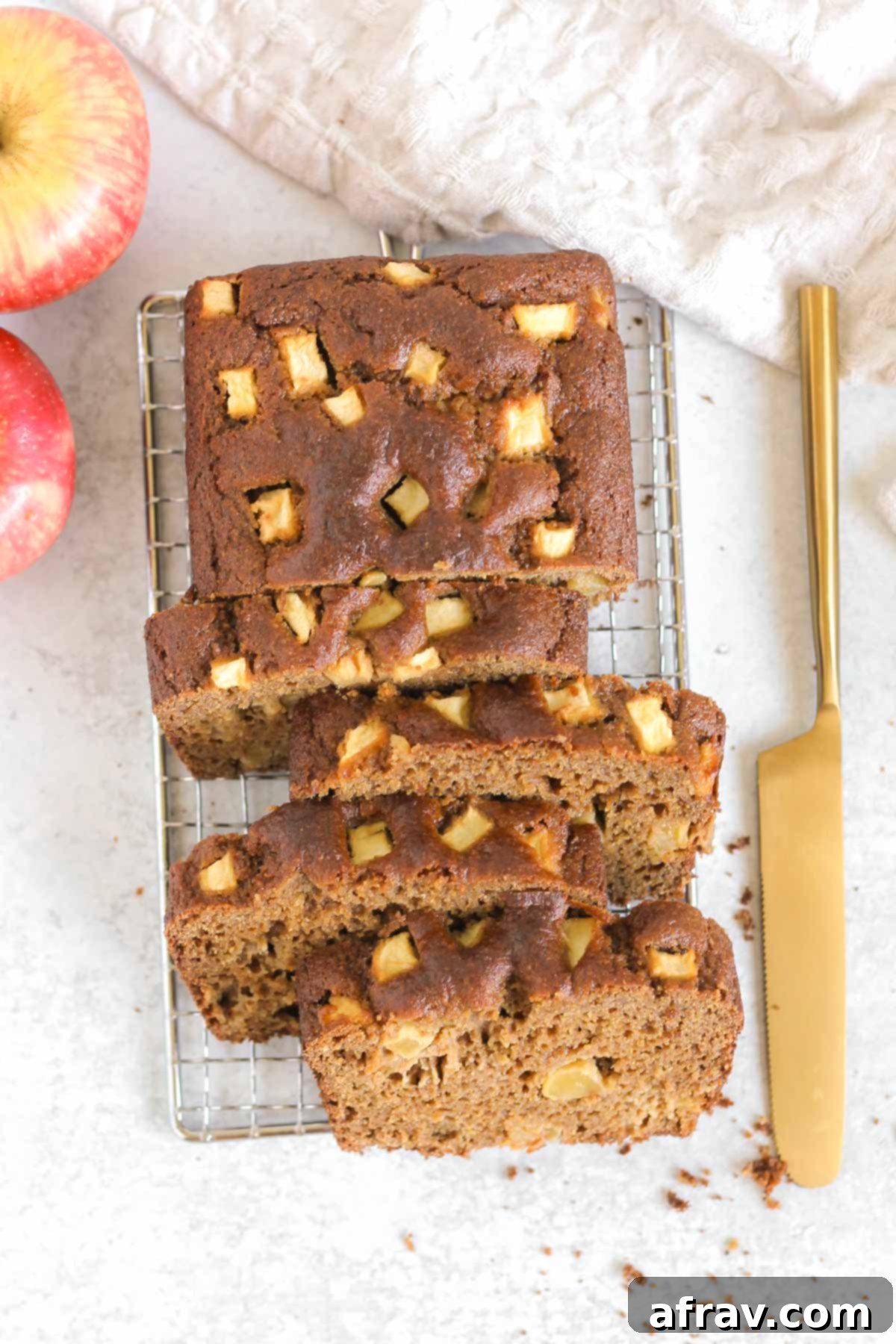 Half sliced loaf of apple bread on a wire cooling rack, showcasing its moist, fluffy texture and warm golden crust.