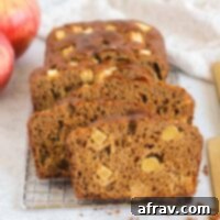 Slices of healthy apple bread on a rectangular wire cooling rack with a gold knife on the side and apples in the background, ready to be served.