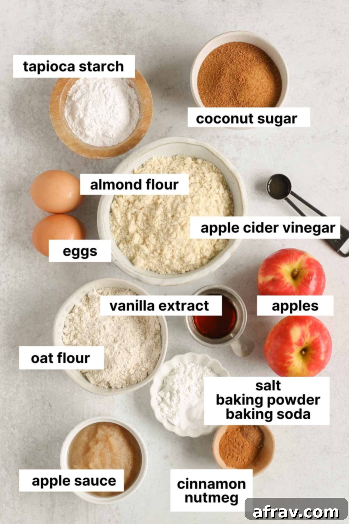 Labeled ingredients for healthy apple bread including almond flour, oat flour, eggs, apples, and spices laid out on a clean surface.