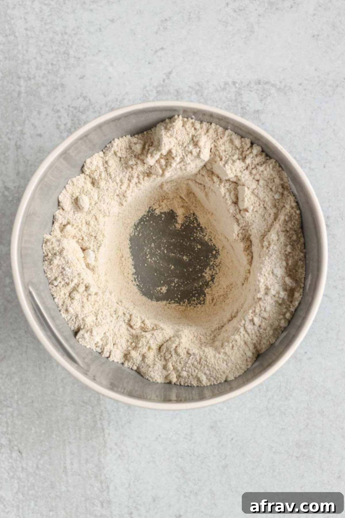 Dry ingredients for apple bread, including almond flour and oat flour, mixed together in a large mixing bowl with a visible well in the center.