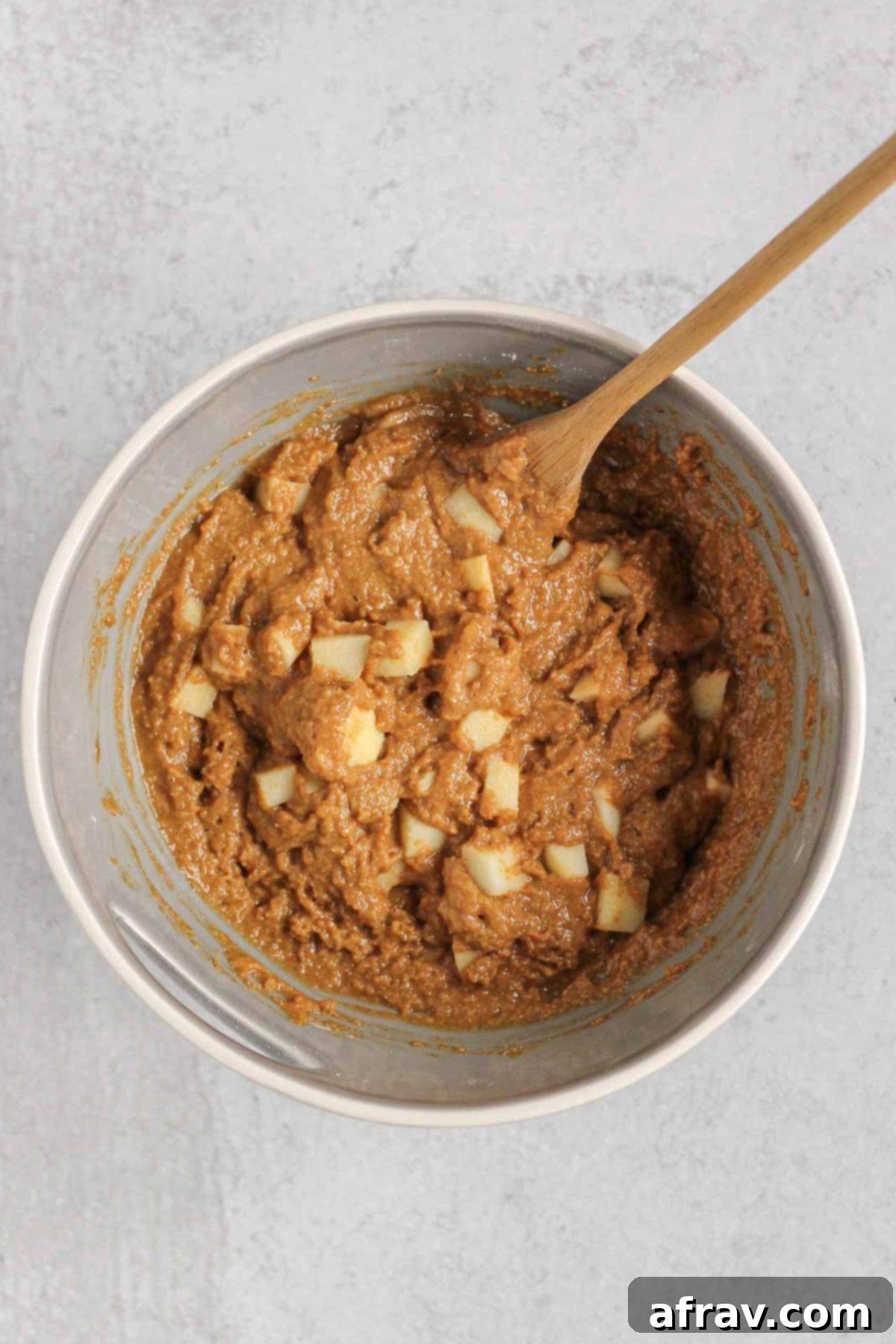 Peeled and chopped apples being gently folded into the apple bread batter in a large mixing bowl with a spatula.