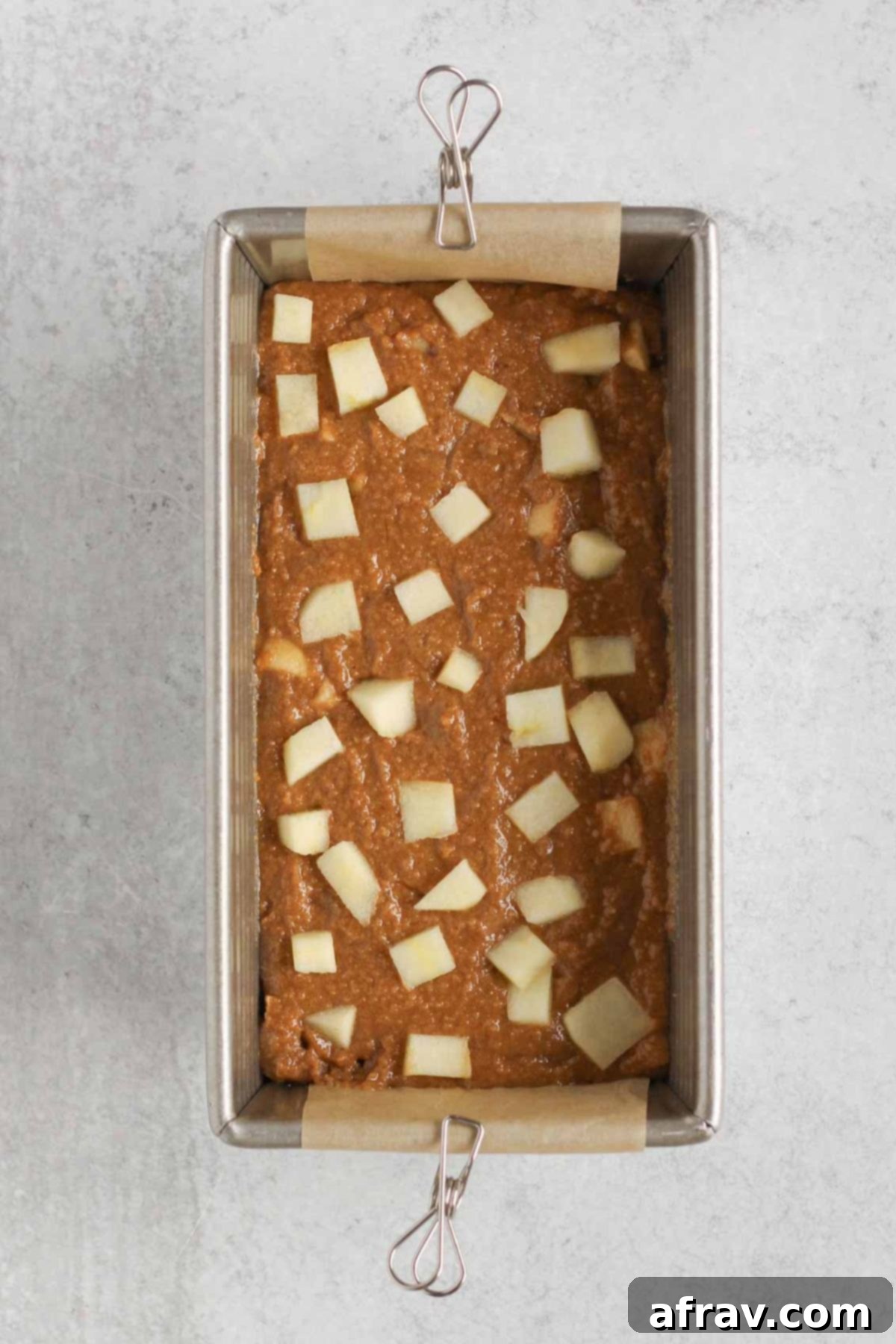 Loaf pan filled with apple bread batter, topped with additional chopped apples for a beautiful presentation before baking.