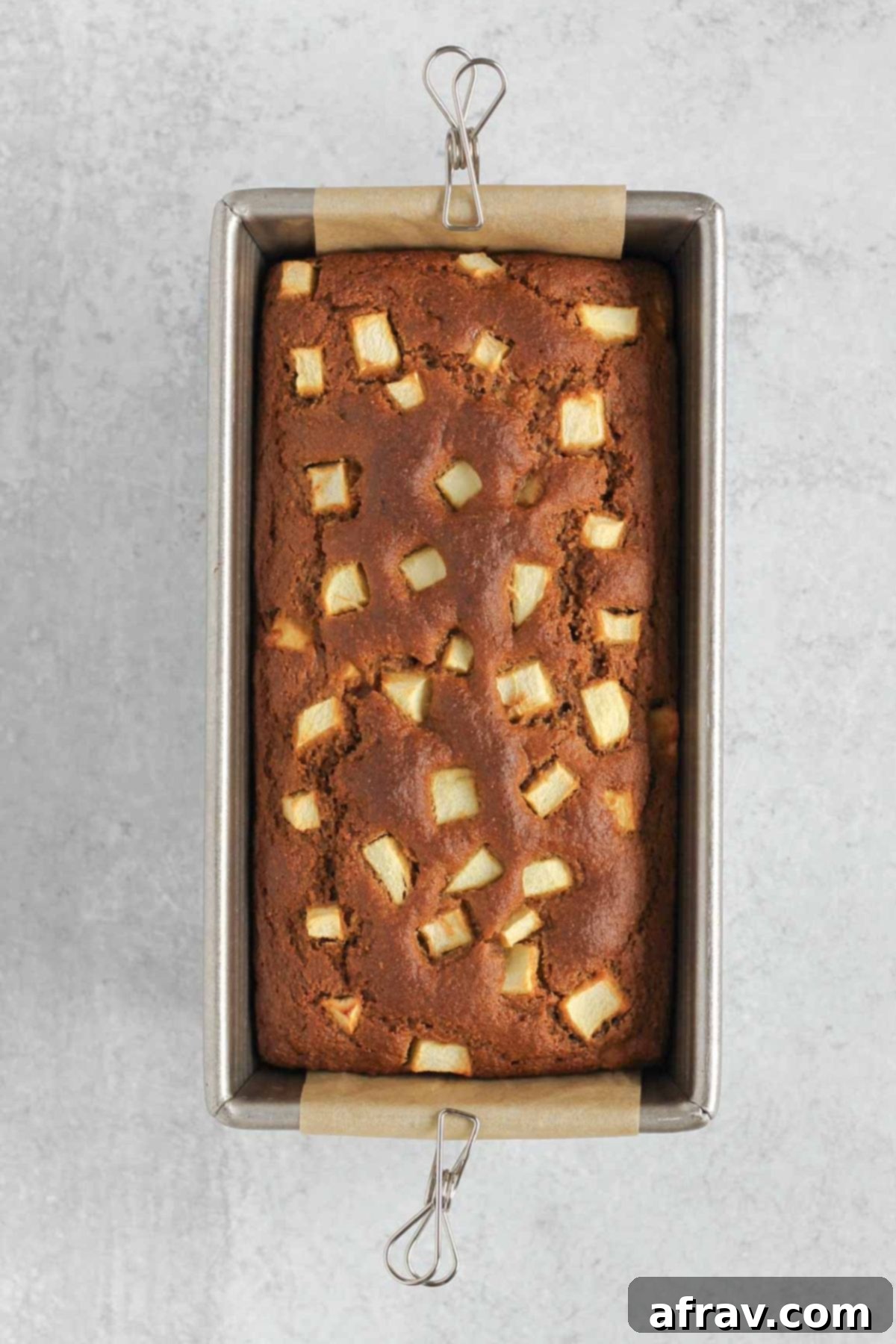 Freshly baked golden-brown loaf of apple bread cooling in its loaf pan after being removed from the oven.