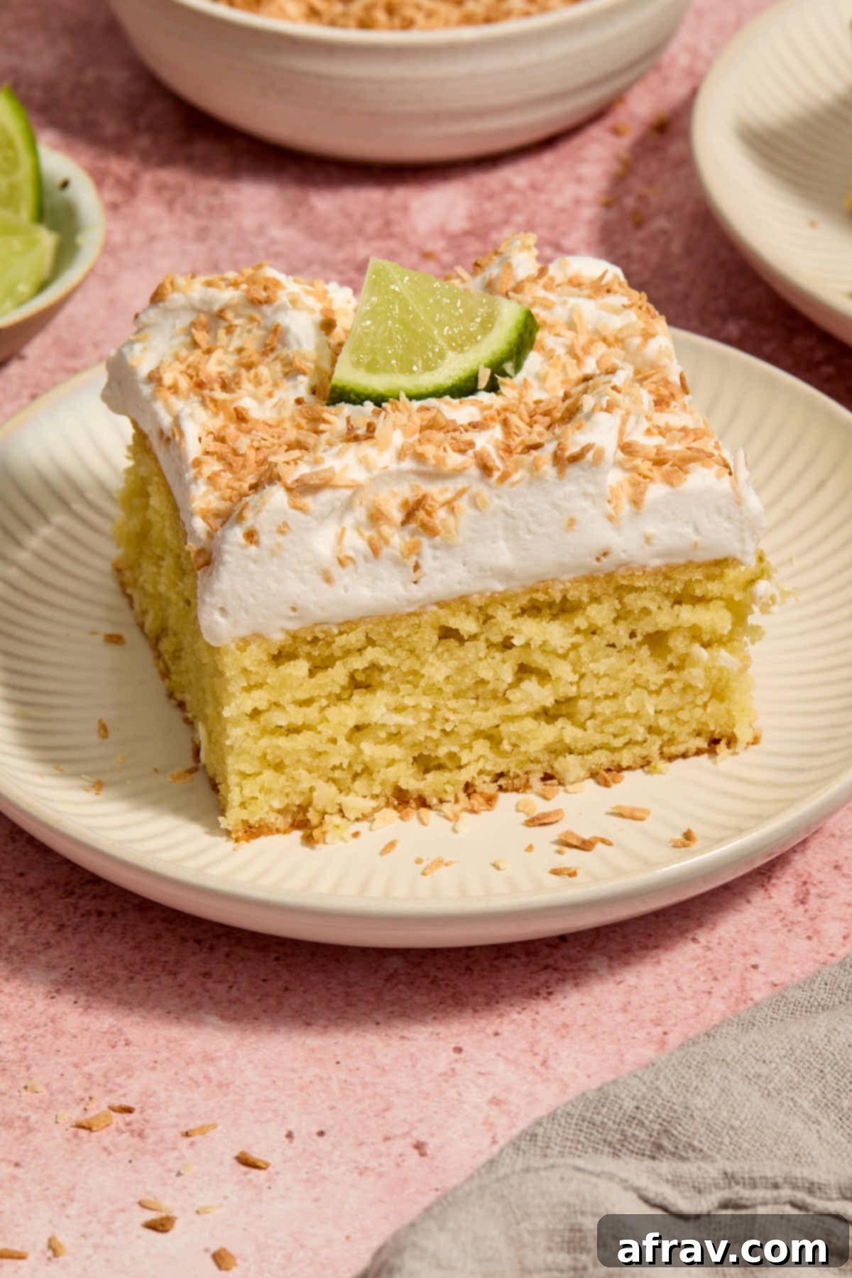 Side view of a perfectly sliced piece of Almond Flour Coconut Lime Cake on a white plate, showcasing its layers and topping.