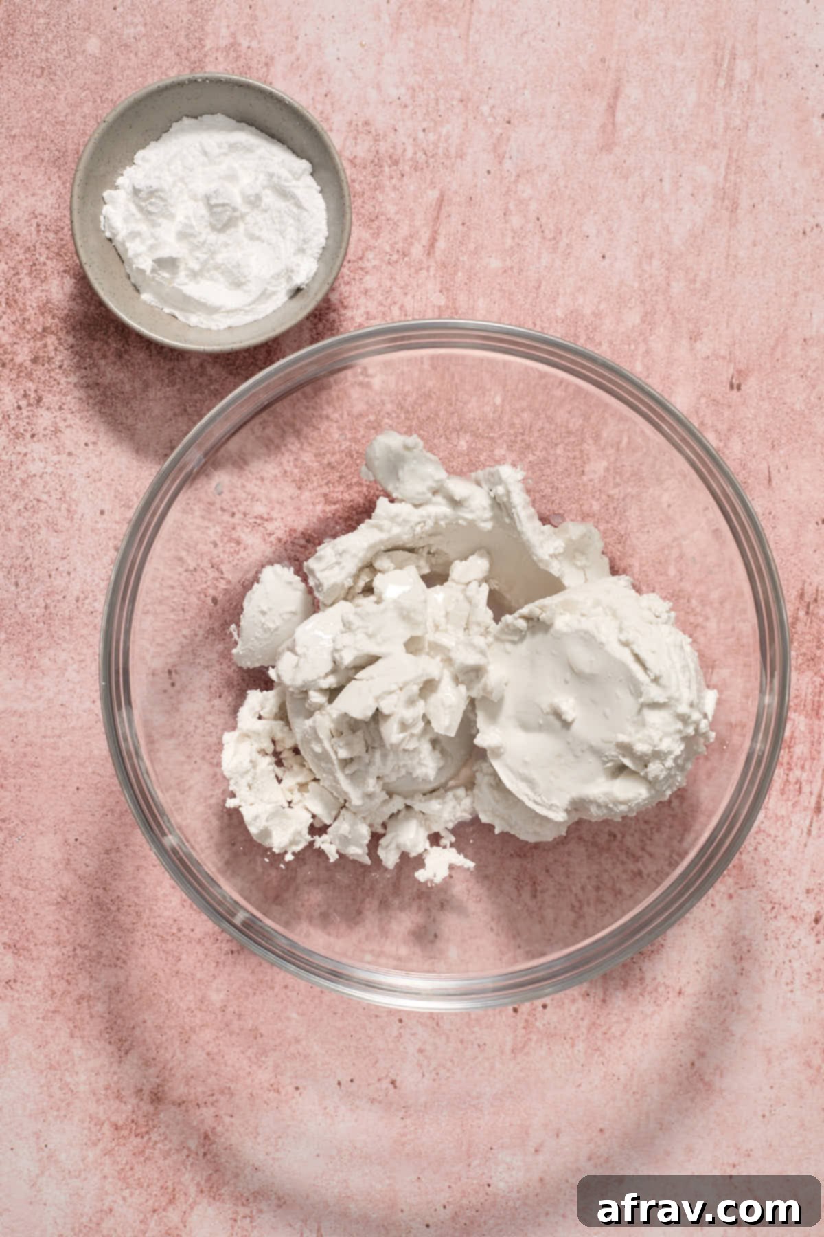 Hardened coconut cream scooped from a can into a glass bowl, ready for whipping, with powdered sugar visible on the side.