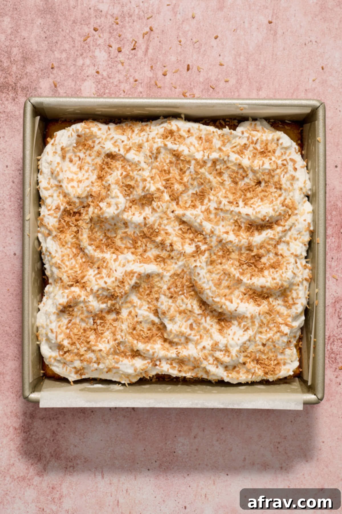 Finished almond flour coconut lime cake in the pan, topped with white coconut whipped cream and golden toasted coconut flakes.