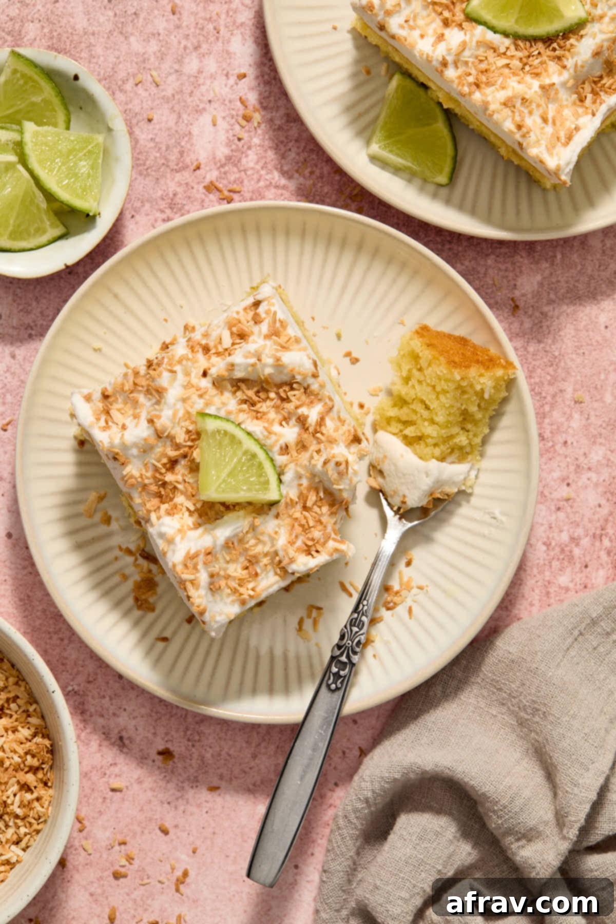 Overhead view of a beautiful slice of almond flour coconut lime cake on a plate with a fork, showing a missing bite and its fluffy texture.