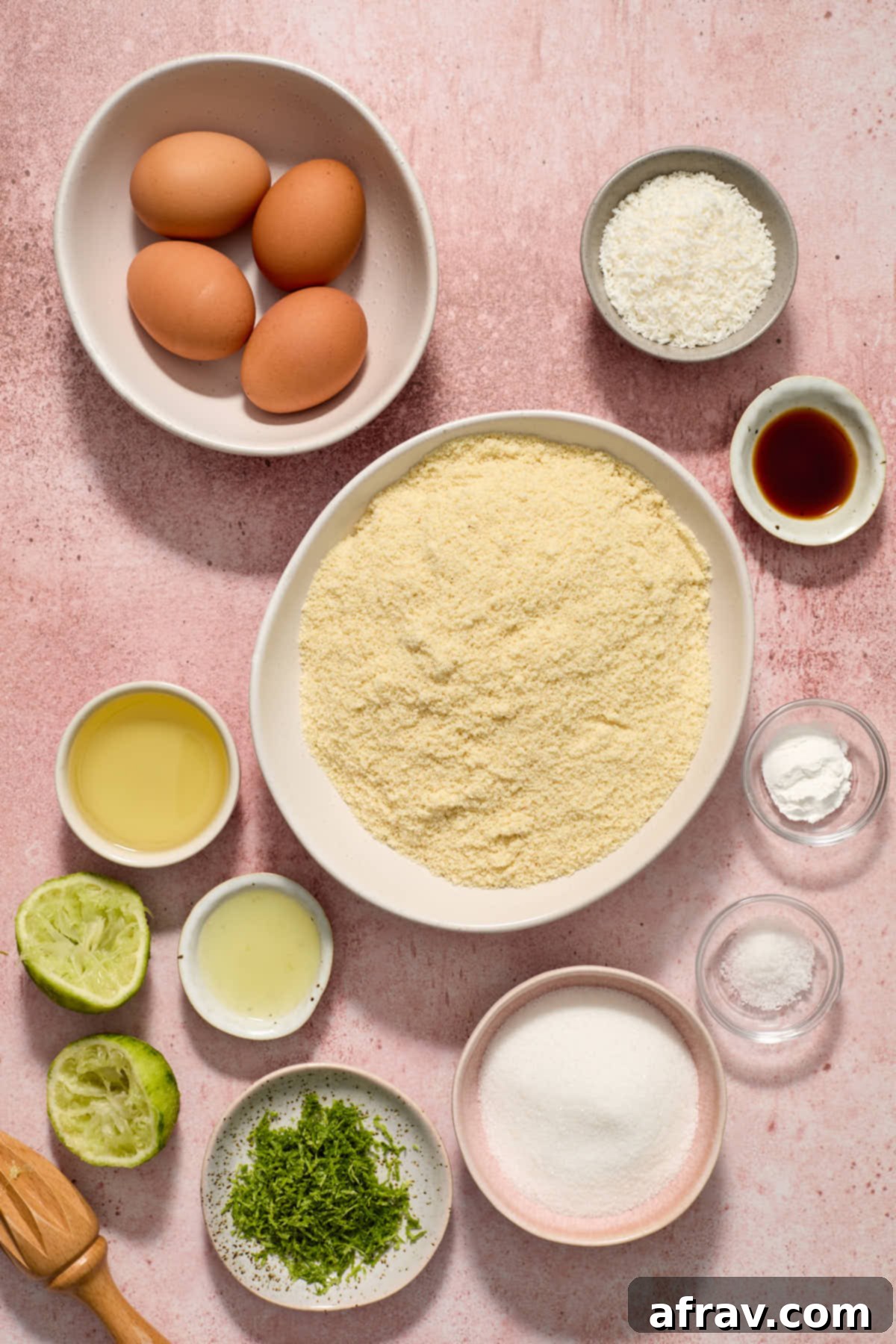 Ingredients for the almond flour coconut lime cake, neatly arranged on a pink surface, including almond flour, limes, eggs, oil, and shredded coconut.