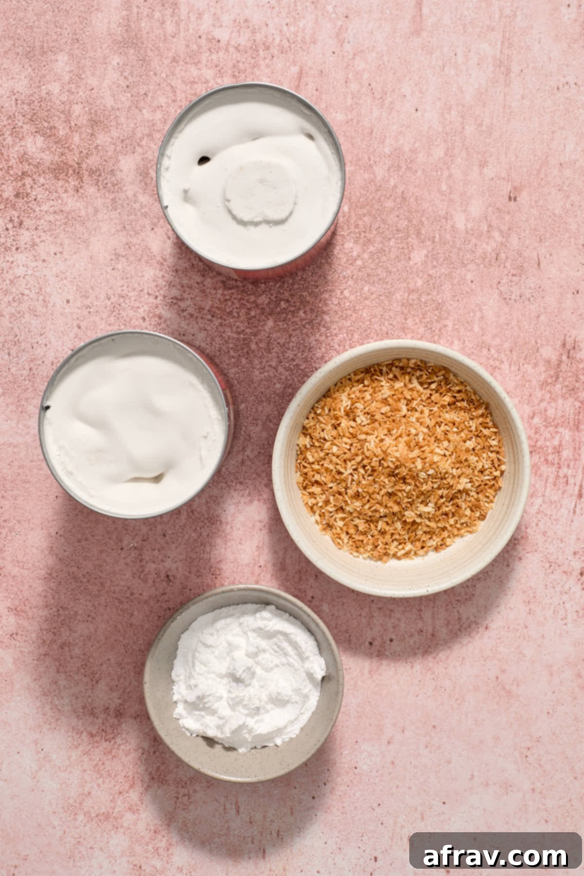 Ingredients for coconut whipped cream, including a can of chilled full-fat coconut milk, powdered sugar, and vanilla extract, on a pink background.