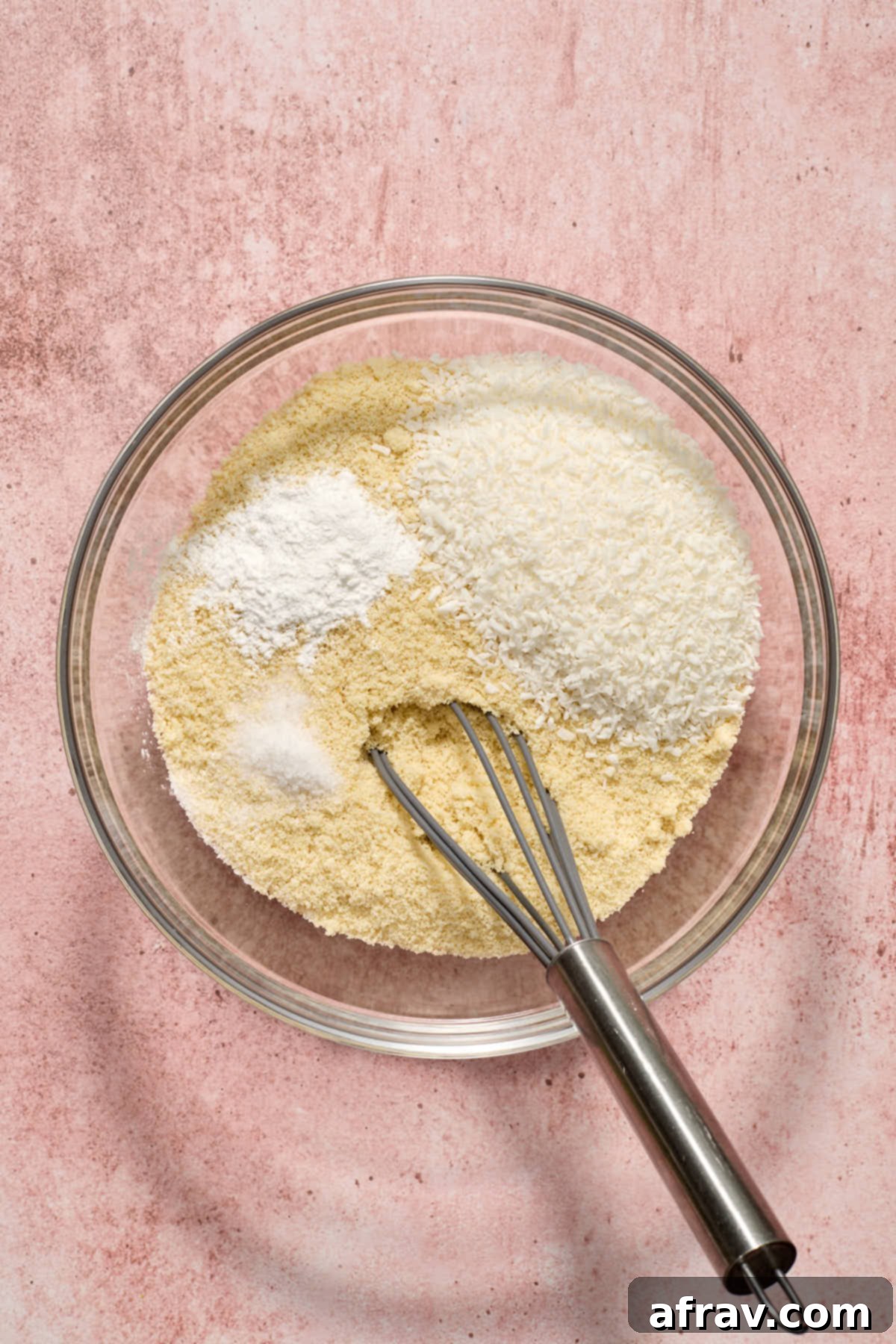 Dry ingredients for almond flour coconut lime cake in a glass bowl with a whisk, including almond flour, shredded coconut, baking powder, and salt.