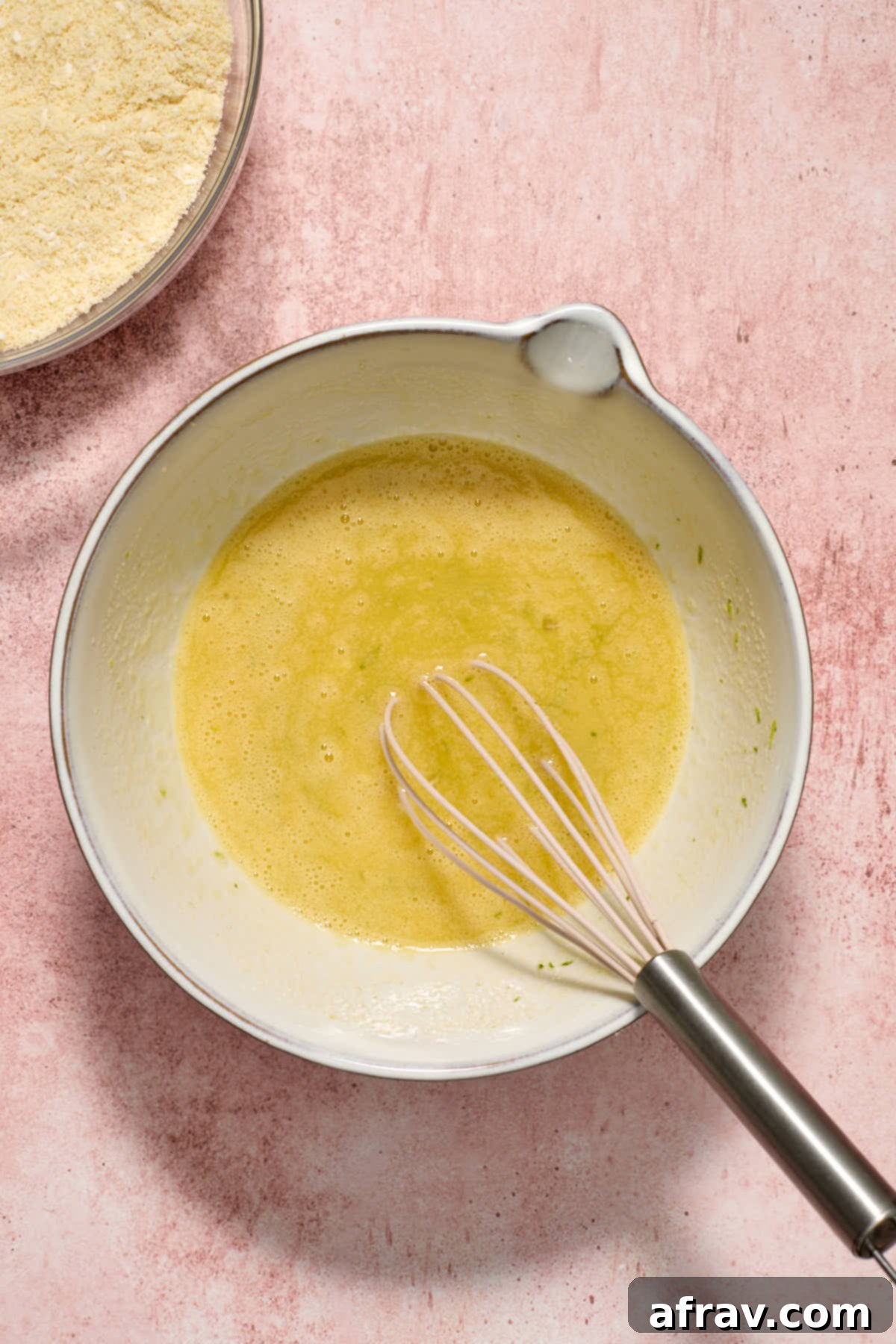 Wet ingredients including eggs, lime-infused sugar, oil, and lime juice whisked together in a white bowl, with the dry ingredient bowl nearby.