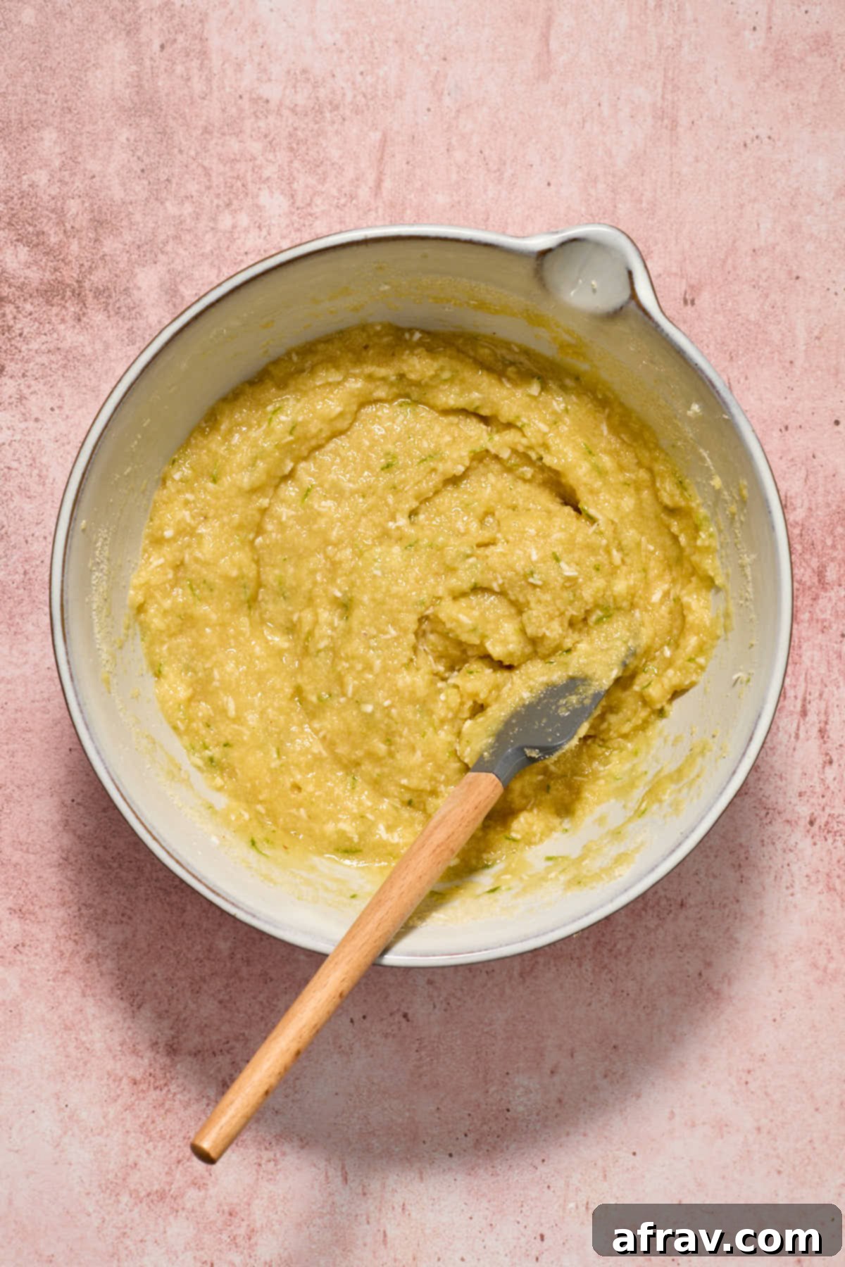 Cake batter being gently folded with a spatula in a white bowl, showing the incorporation of dry ingredients into wet.
