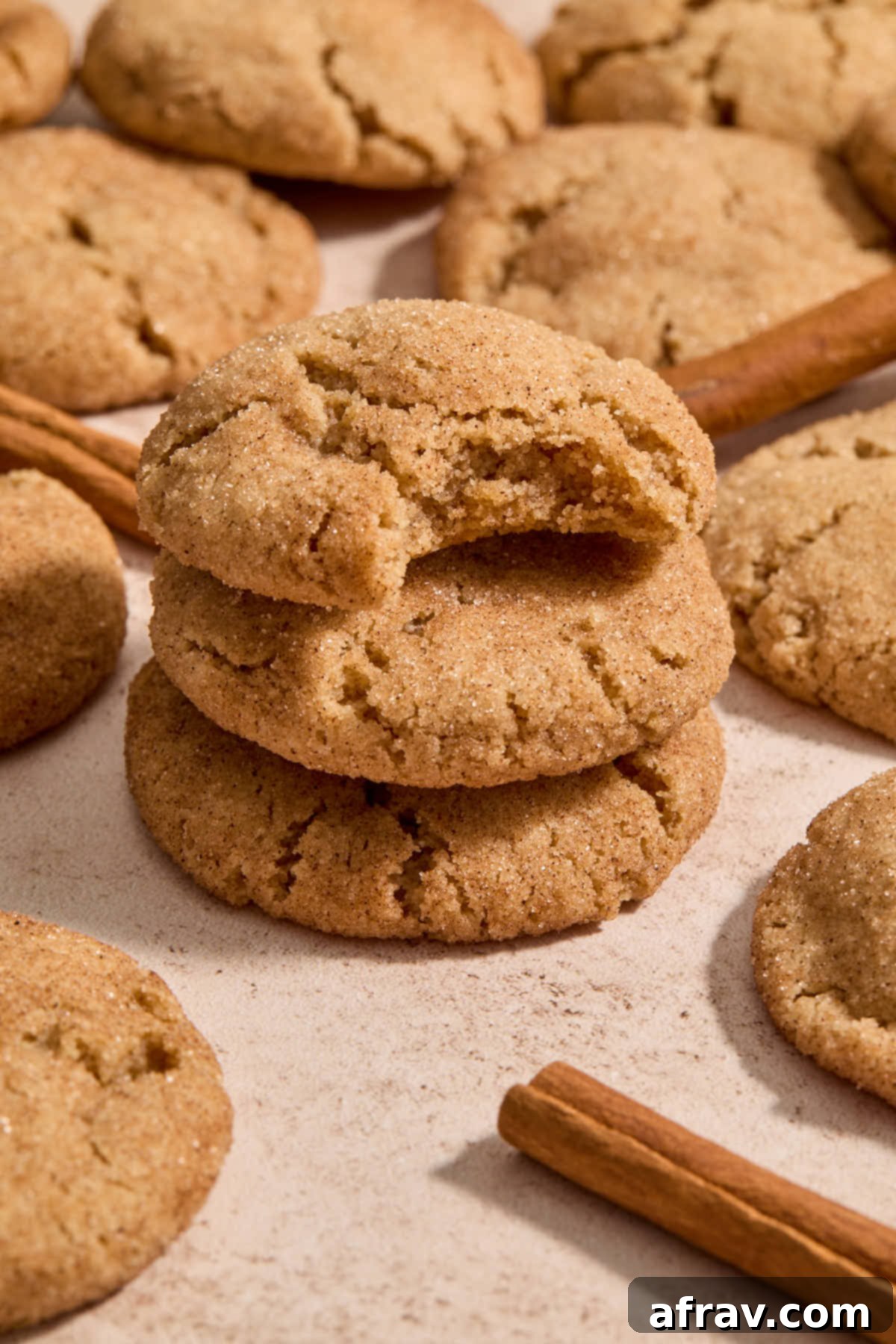 Stack of soft and chewy almond flour snickerdoodle cookies with a bite taken out of the top one, showing its tender interior and crackled cinnamon sugar exterior.