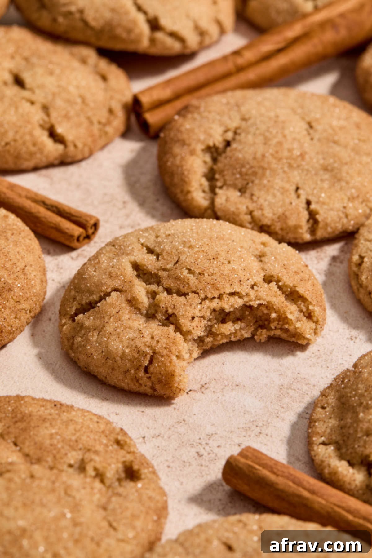 A beautiful arrangement of baked almond flour snickerdoodles with cinnamon sticks, one cookie showing a bite taken out of it.