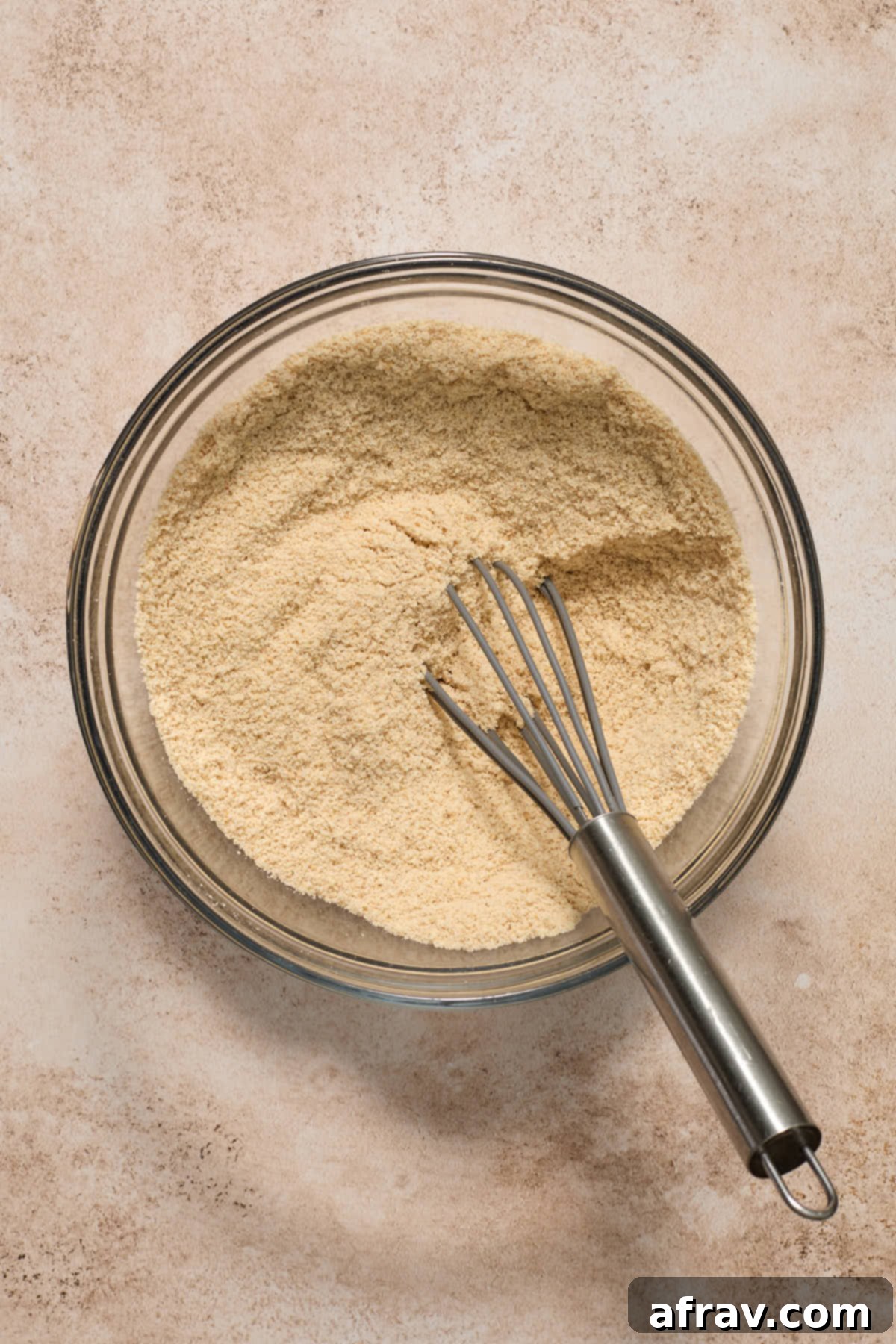 Dry cookie ingredients like almond flour, cornstarch, cinnamon, baking soda, cream of tartar, and salt, whisked together in a glass bowl.