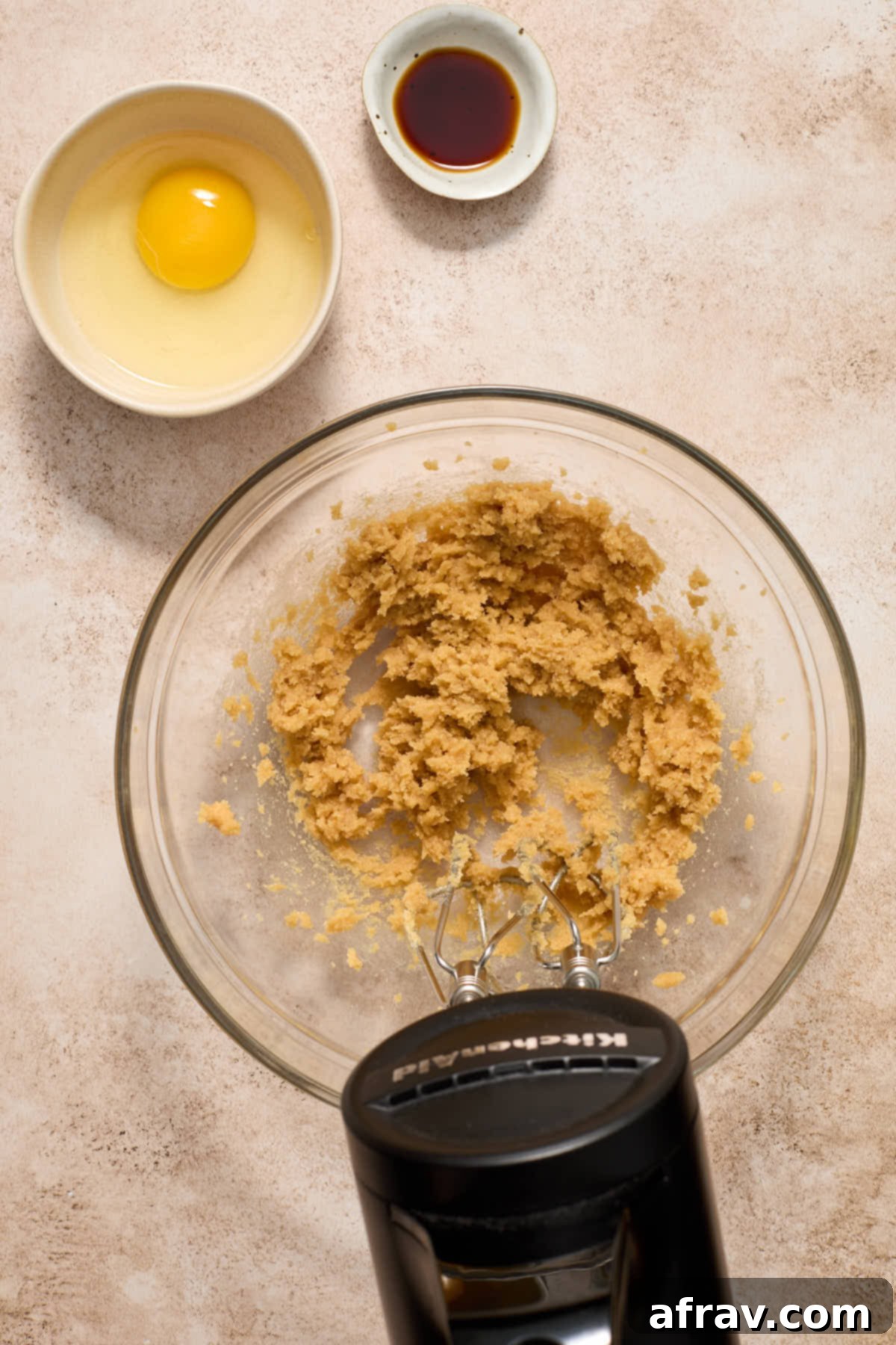 Creamy mixture of softened butter and sugars in a bowl, with a separate bowl holding egg and vanilla extract.