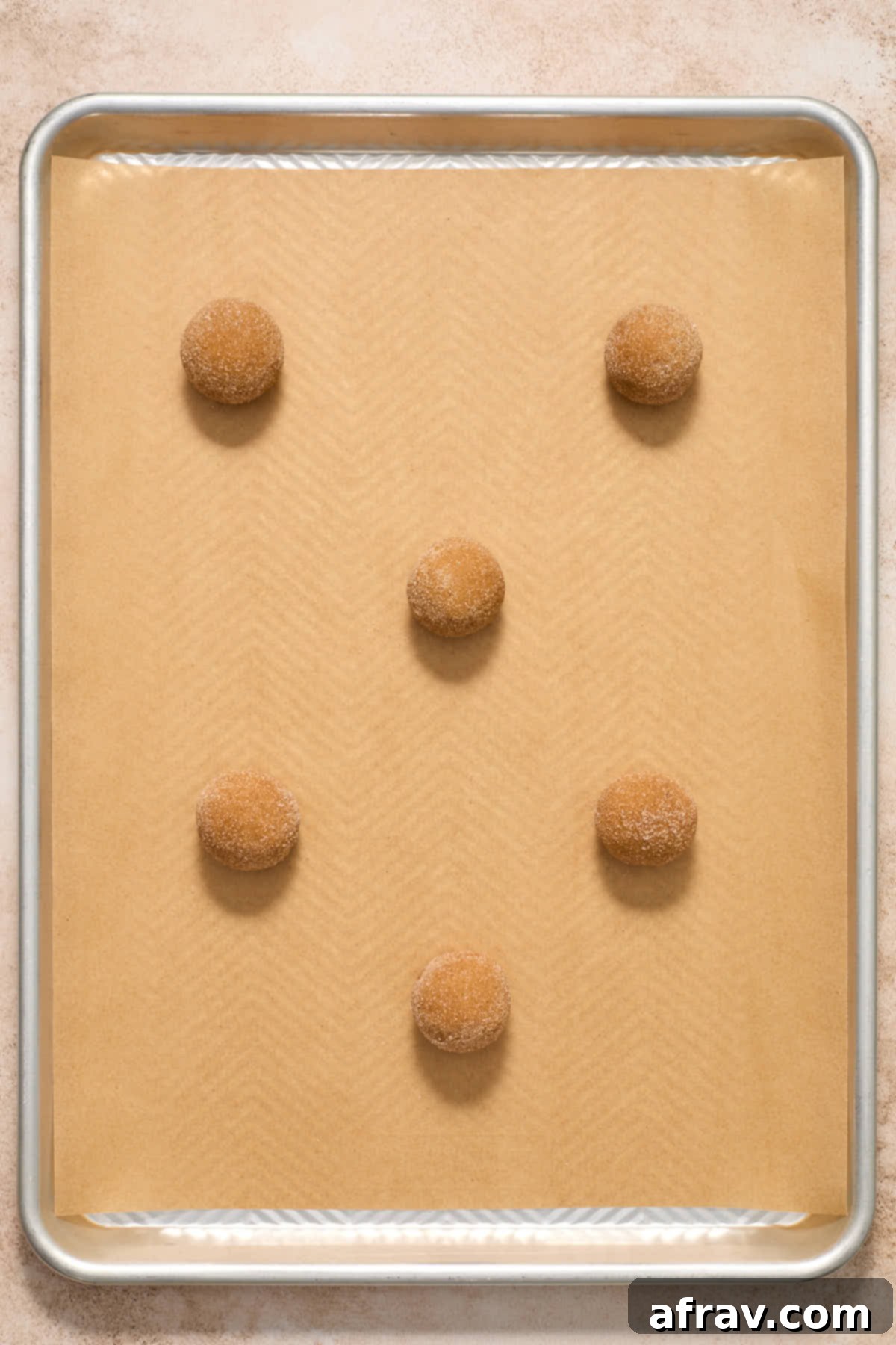 Uniform cookie dough balls rolled in cinnamon sugar and neatly arranged on a parchment-lined baking sheet.
