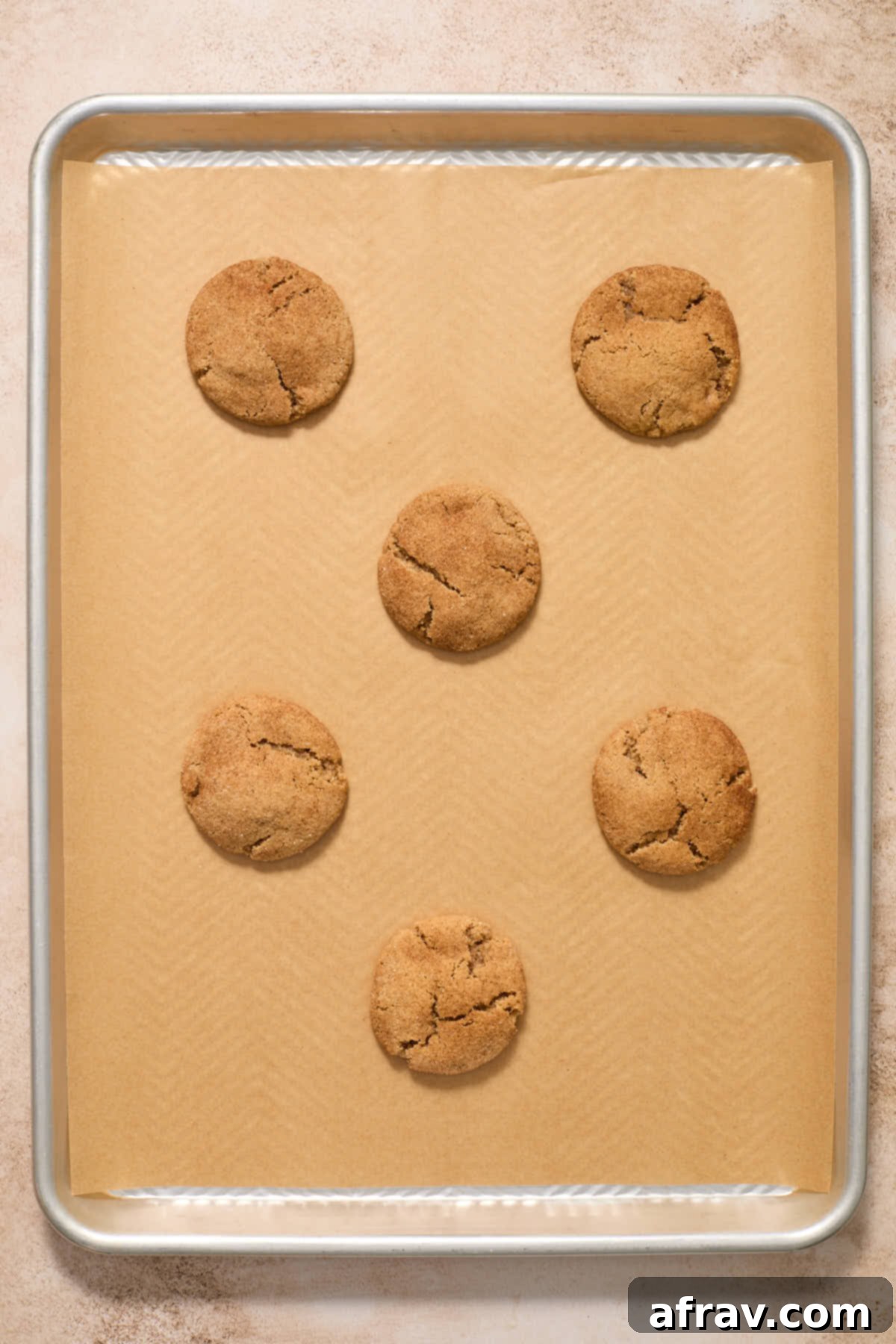 Freshly baked snickerdoodles cooling on a baking sheet, showing their puffy, crackled tops.