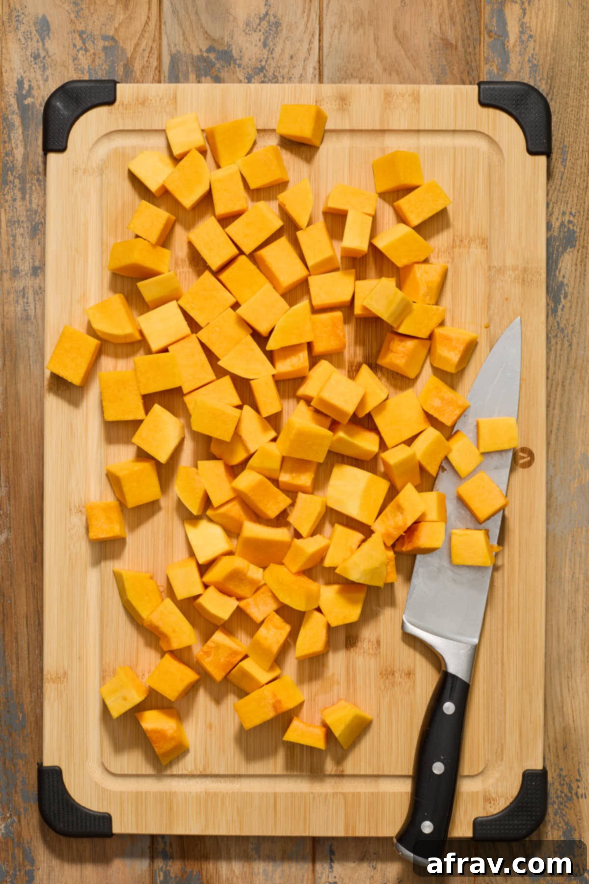 Freshly peeled, cut, and uniformly cubed butternut squash on a rustic wooden cutting board, with a chef's knife beside it, ready for cooking and culinary exploration.