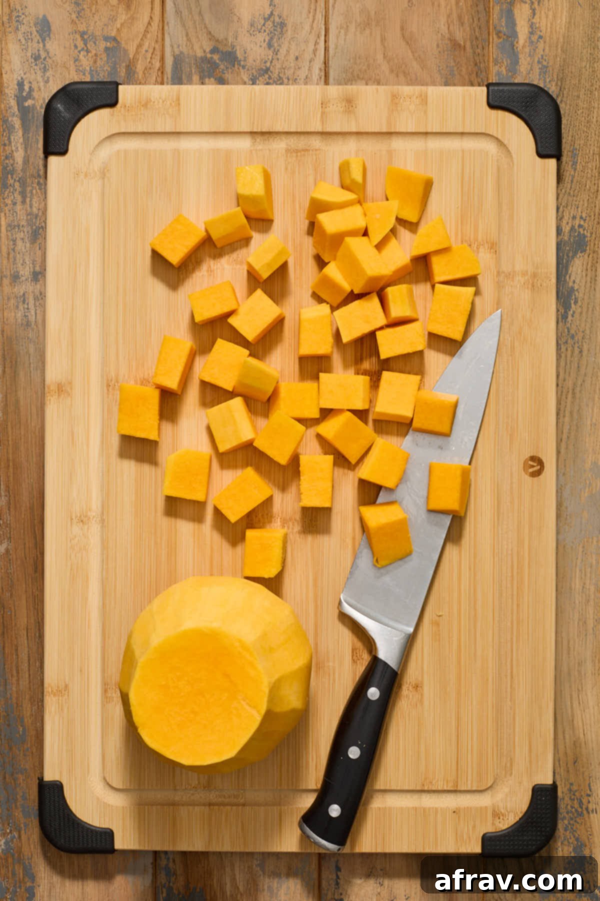 Neatly arranged butternut squash strips from the neck section, now precisely cut into even cubes on a wooden cutting board.