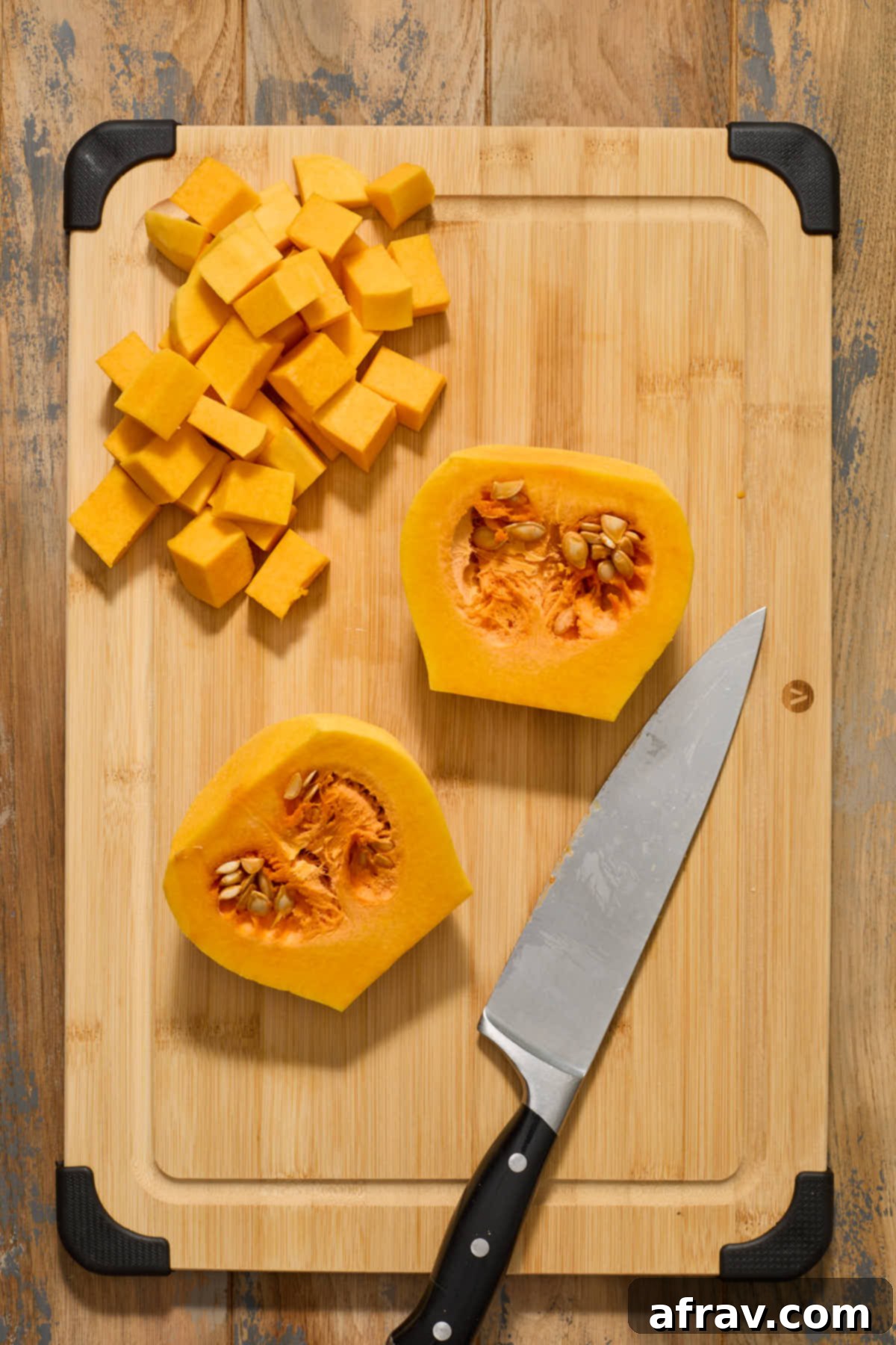 The bulbous bottom half of a peeled butternut squash, cut lengthwise to expose the central cavity filled with seeds and stringy pulp.