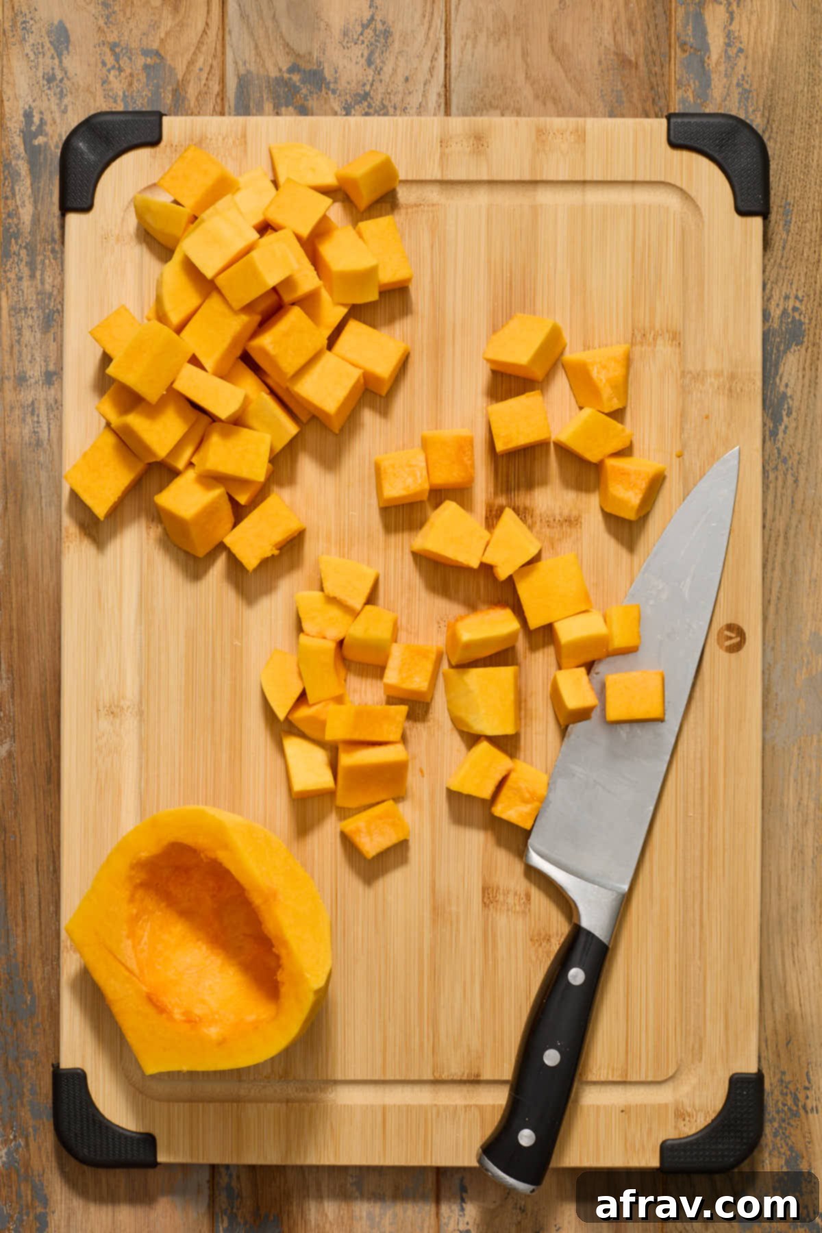 Half-moon slices of butternut squash from the body section, now further cut into even, bite-sized cubes on a wooden cutting board.