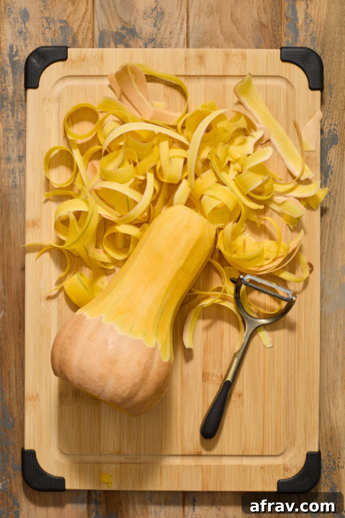 The neck section of the butternut squash, now completely peeled to reveal its smooth, bright orange flesh, resting on a cutting board.