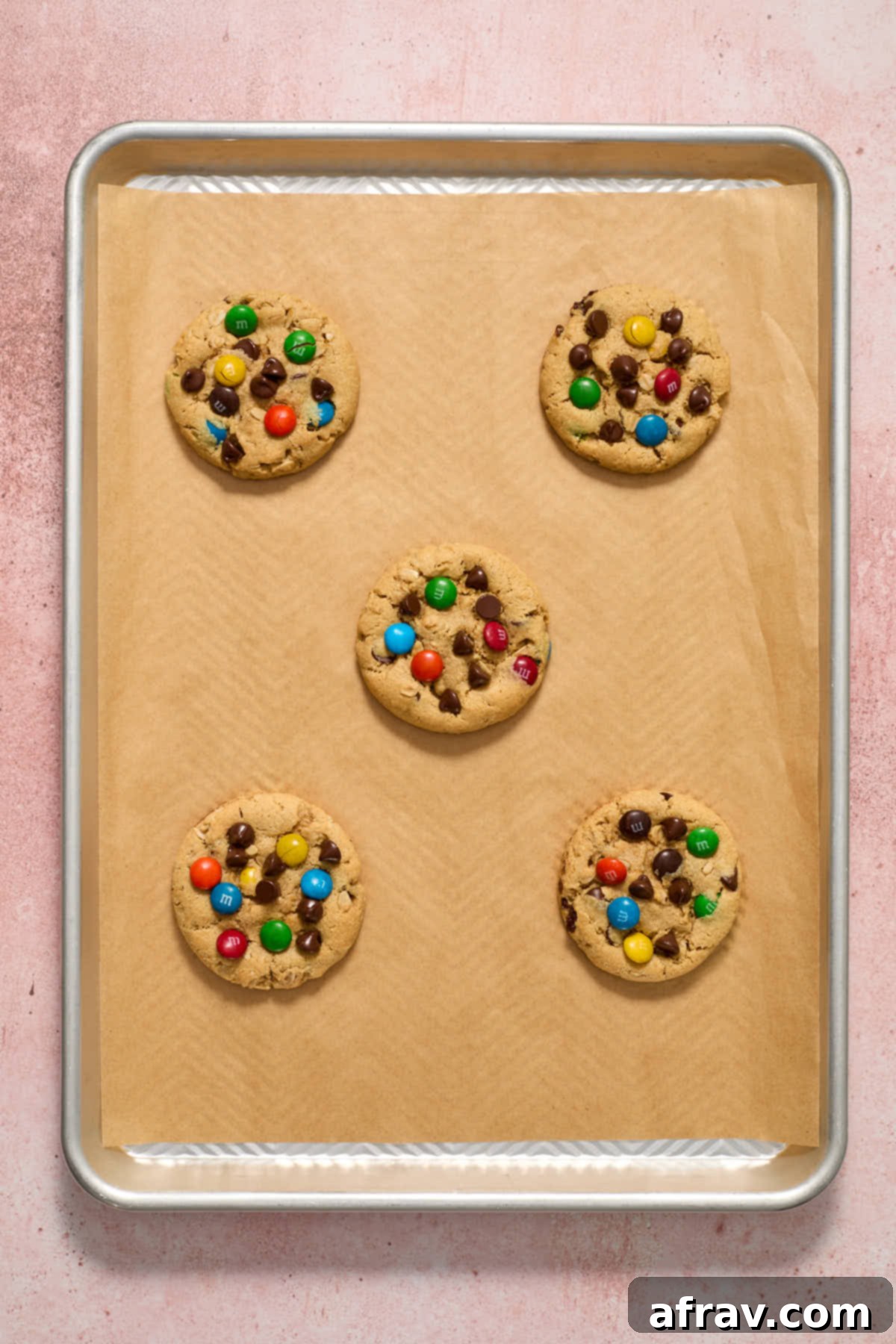 Baked monster cookies cooling on a baking sheet, golden brown with visible M&Ms and chocolate chips.
