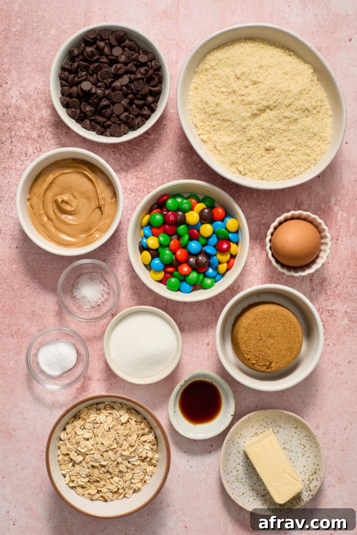Ingredients for almond flour monster cookies laid out in individual bowls: peanut butter, butter, sugars, almond flour, oats, chocolate chips, M&Ms, egg, and vanilla.
