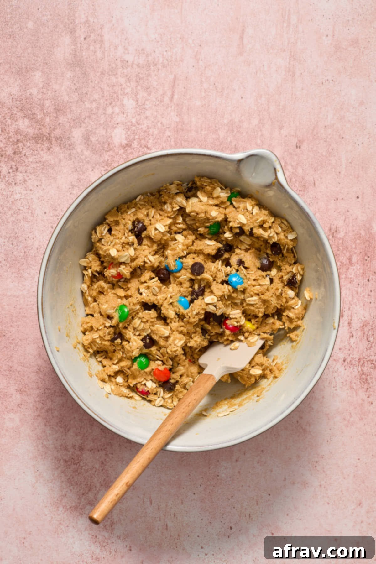 Fully mixed cookie dough in a bowl, now containing oats, M&Ms, and chocolate chips evenly distributed.
