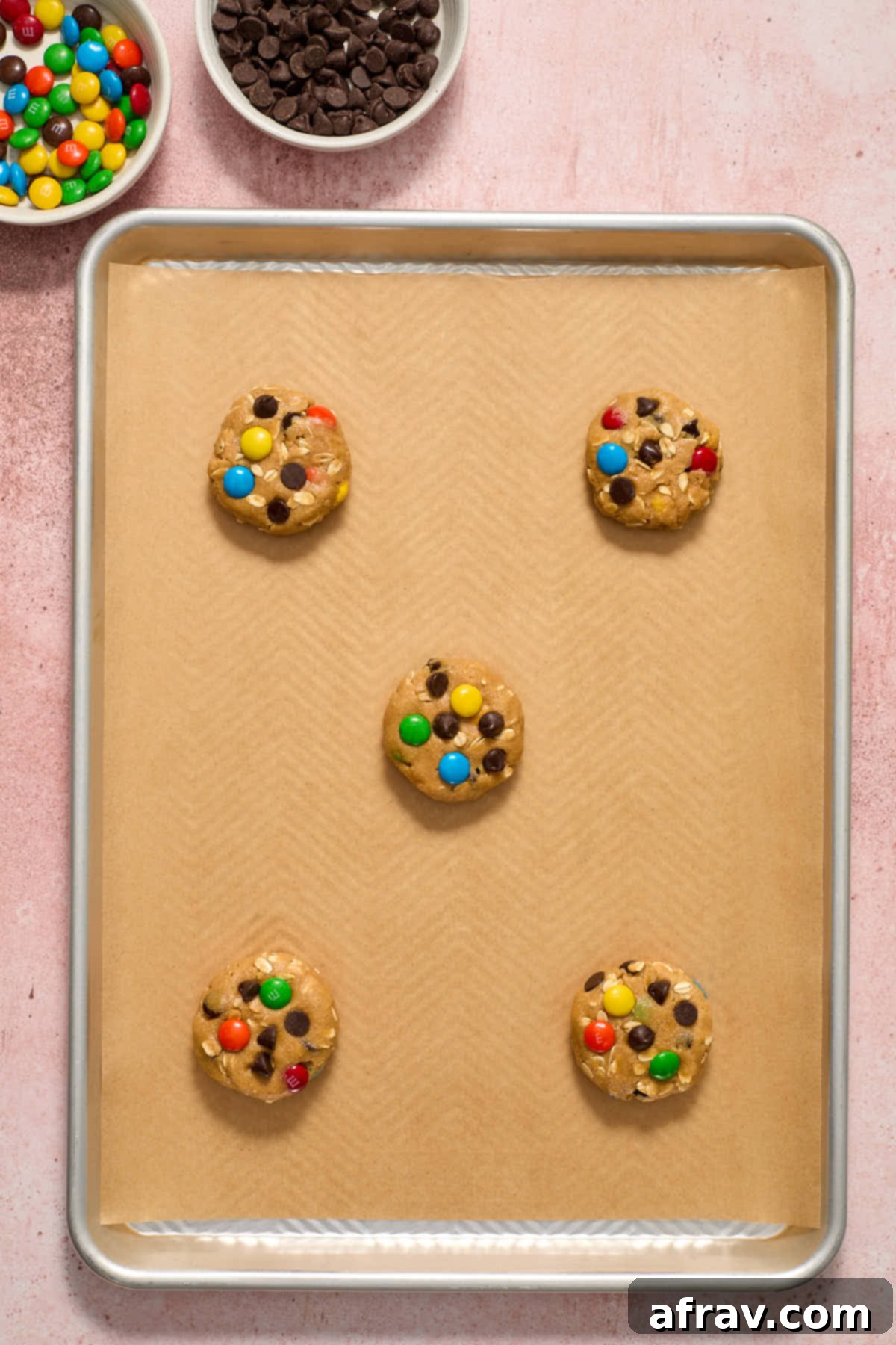 Cookie dough balls slightly flattened with M&Ms and chocolate chips pressed into their tops.
