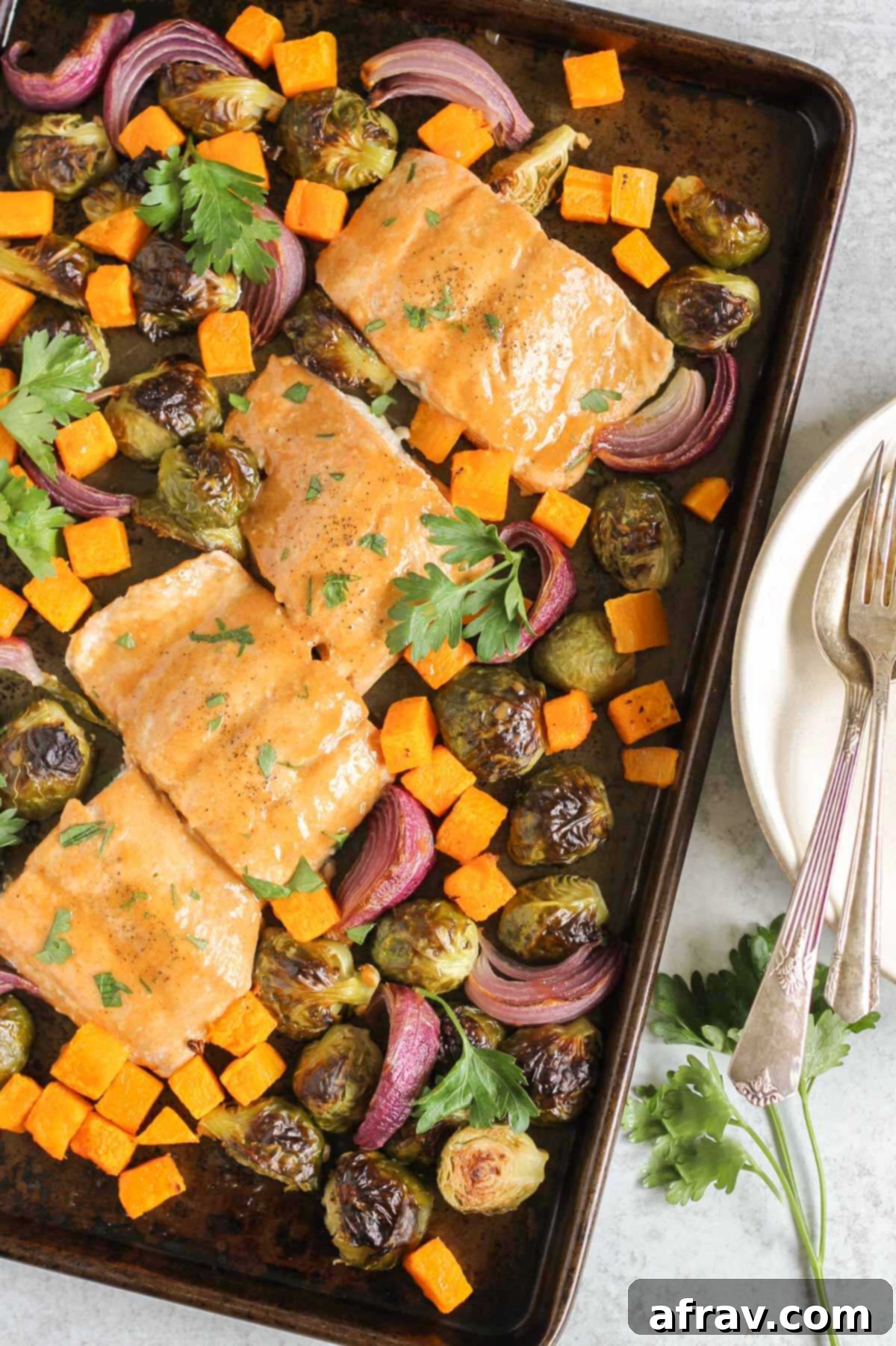 Sheet Pan Maple Dijon Salmon Dinner 2 Baking pan with cooked salmon fillets with maple dressing, roasted Brussels sprouts, roasted sweet potatoes, and roasted onions.