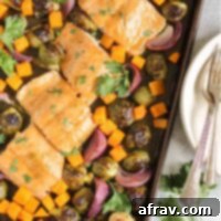 Sheet Pan Maple Dijon Salmon Dinner 10 Baking pan with cooked salmon fillets with maple dressing, roasted Brussels sprouts, roasted sweet potatoes, and roasted onions.