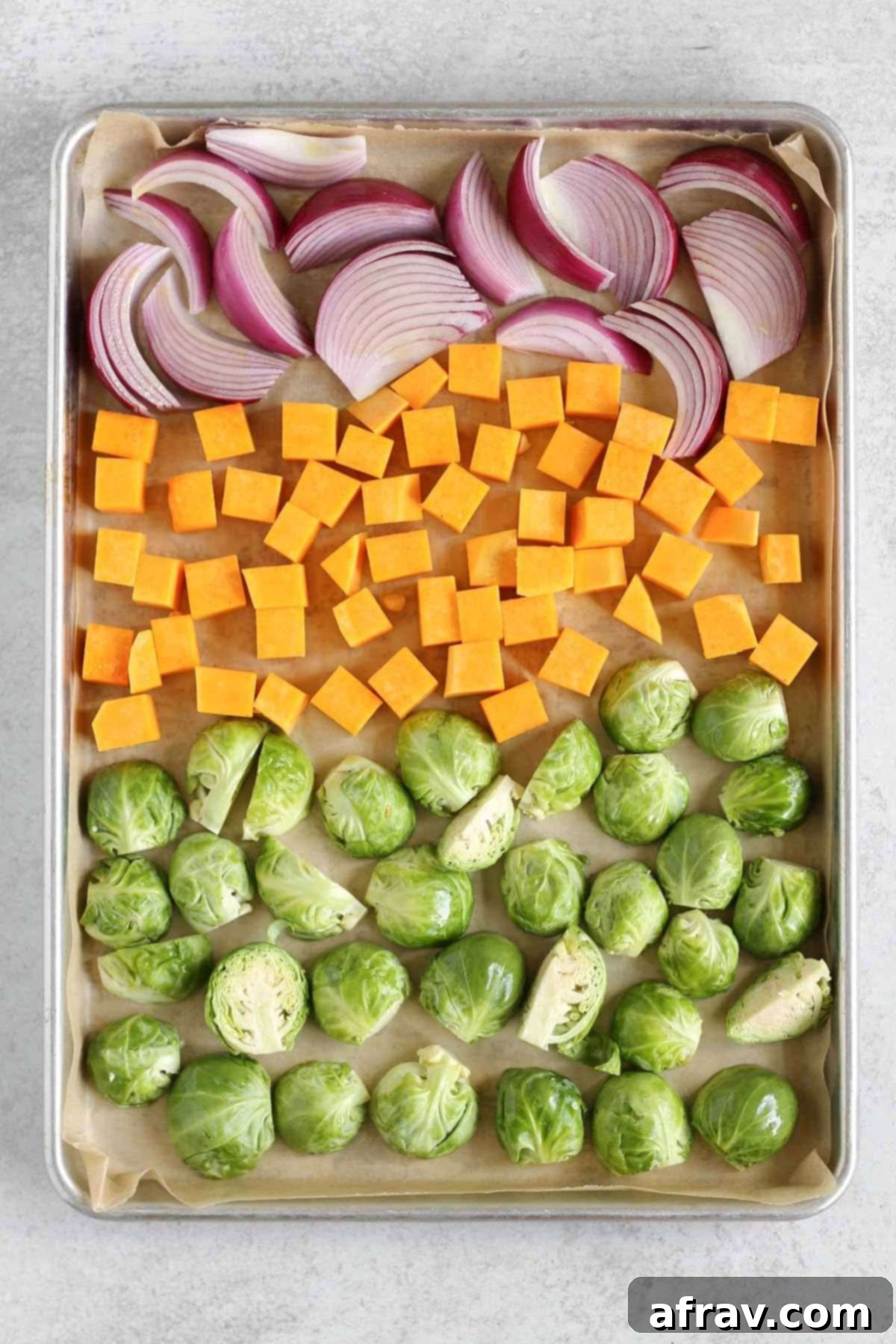 Sheet Pan Maple Dijon Salmon Dinner 4 Baking sheet with raw Brussels sprouts, cubed sweet potatoes, and sliced red onions.