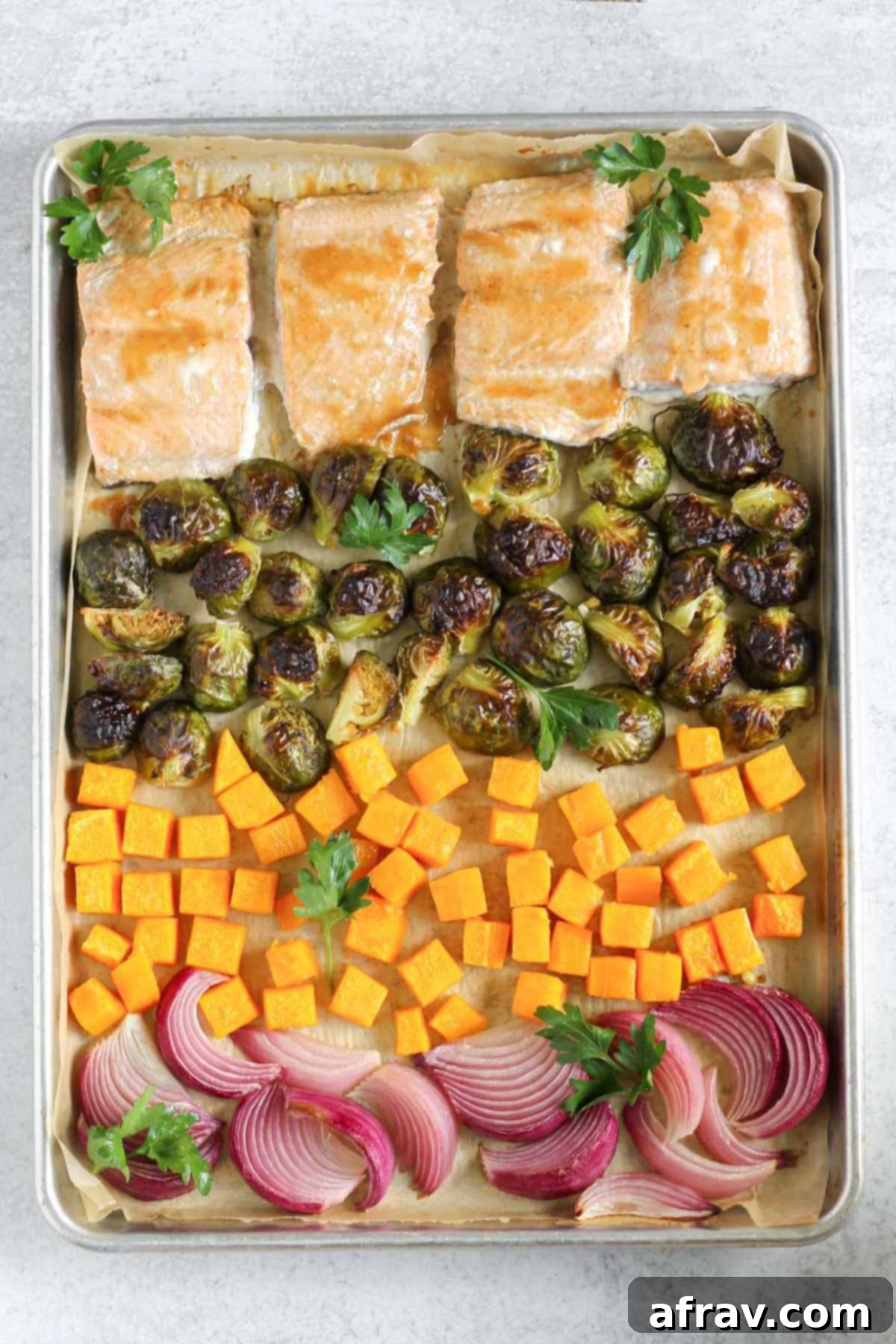 Sheet Pan Maple Dijon Salmon Dinner 7 Baking sheet with with cooked salmon fillets, roasted Brussels sprouts, roasted sweet potatoes, and roasted onions.