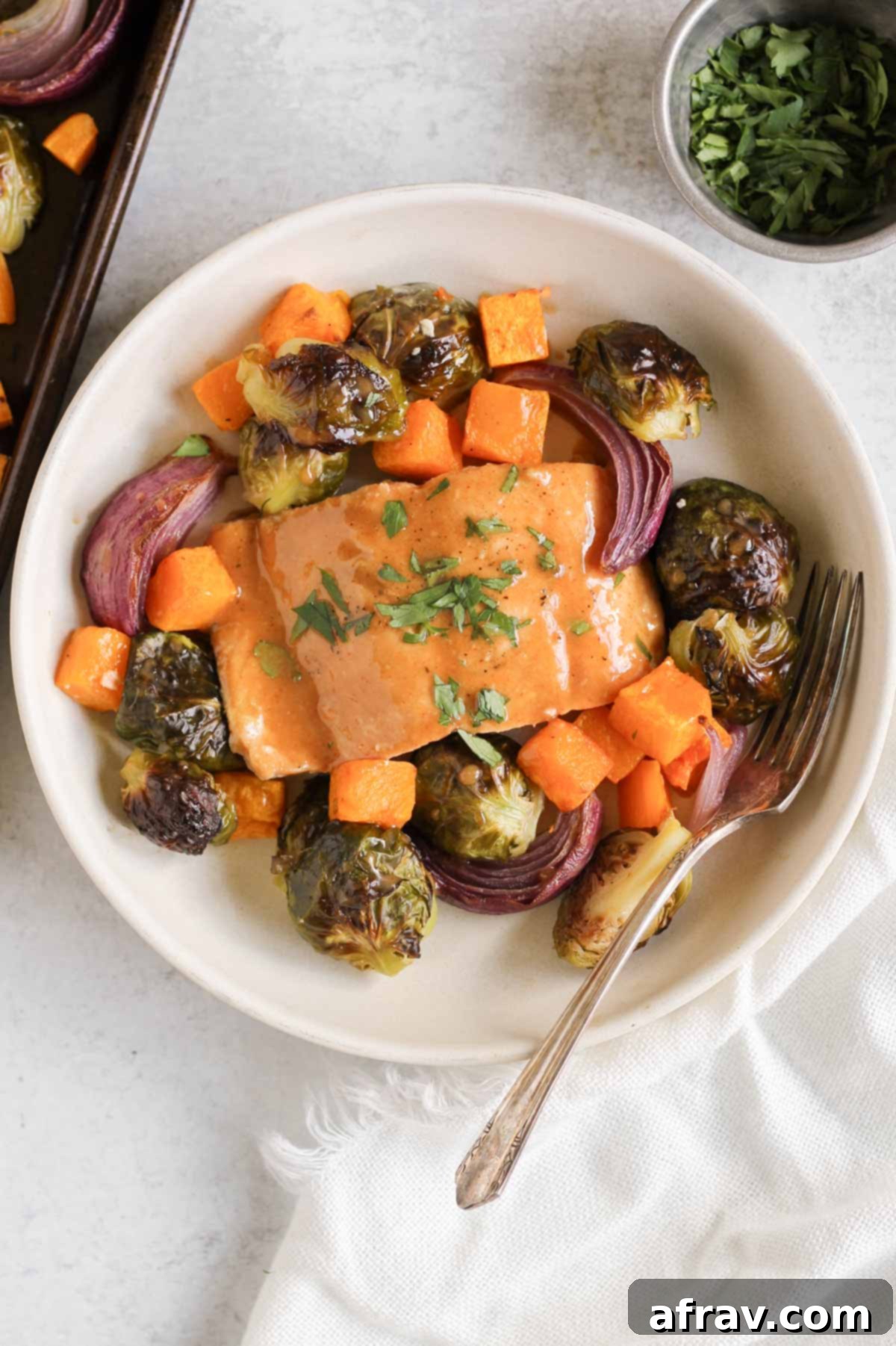 Sheet Pan Maple Dijon Salmon Dinner 9 Single salmon fillet sprinkled with parsley with roasted veggies around the filet sitting in a shallow single serve bowl.