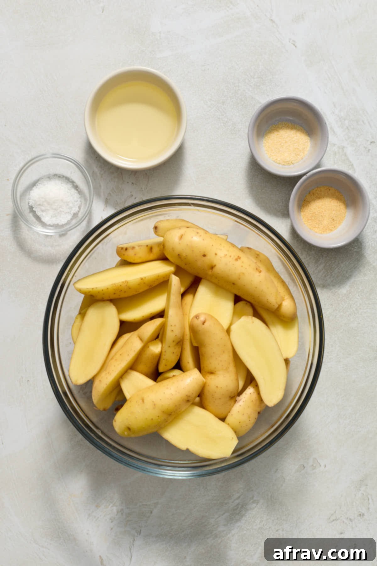 Fingerling potatoes sliced lengthwise in a bowl with oil and seasonings on the side.
