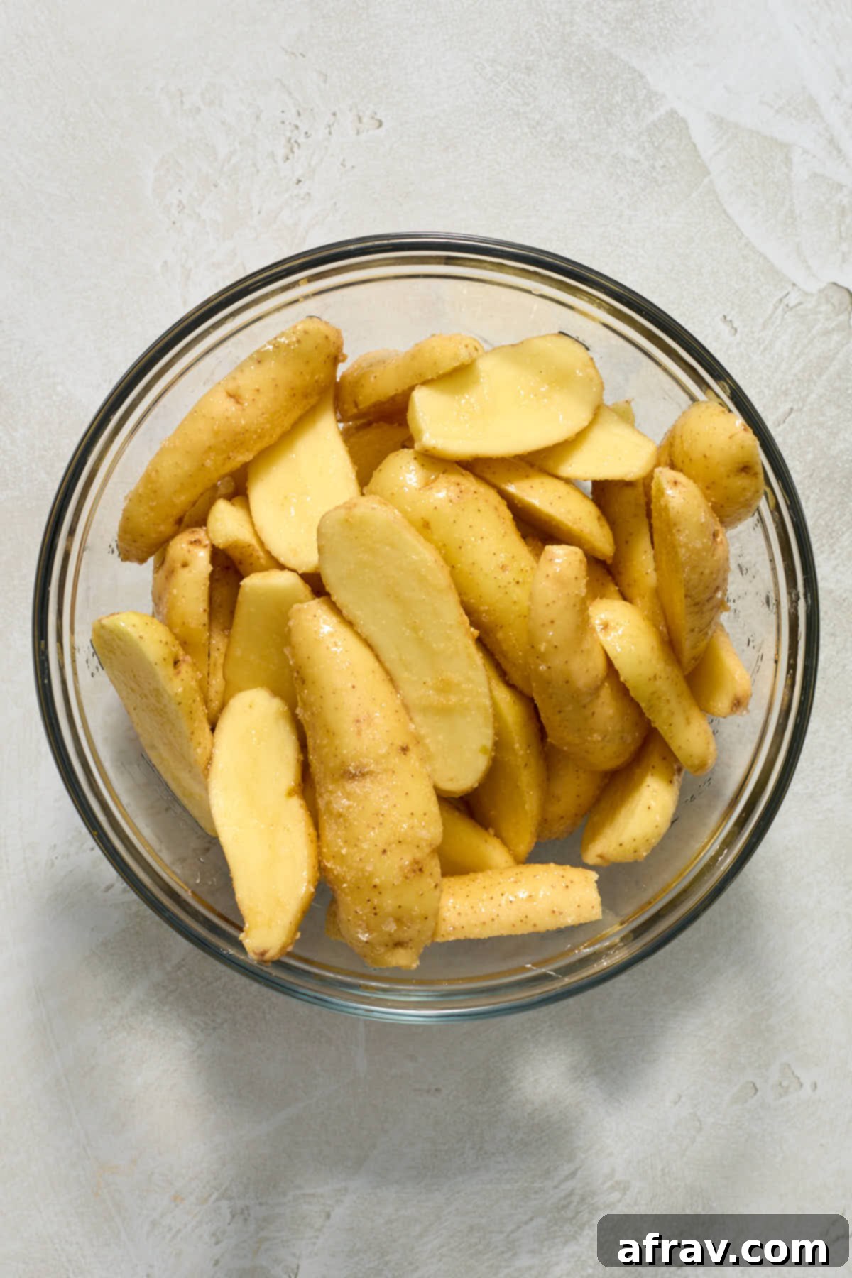 Sliced and seasoned potatoes in a glass bowl.