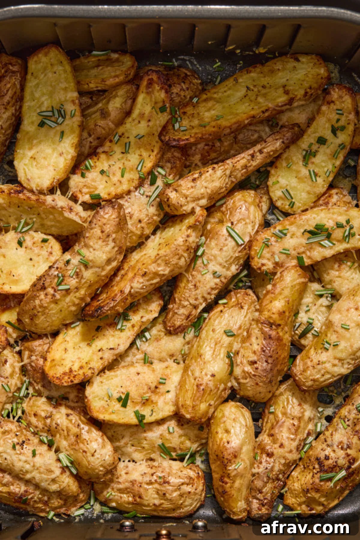 Close up of fingerings in air fryer basket topped with chopped fresh rosemary.