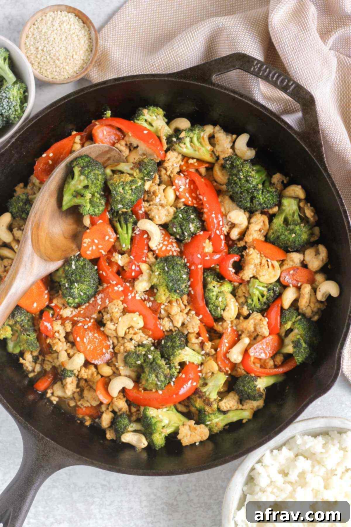 Ground chicken stir fry sprinkled with sesame seeds and cashews in a cast iron skillet with a wooden serving spoon scooping some out.