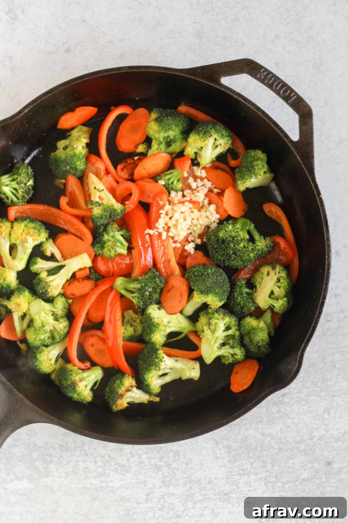 Sautéed broccoli, red peppers, and sliced carrots with fresh garlic and ginger in a cast iron skillet.