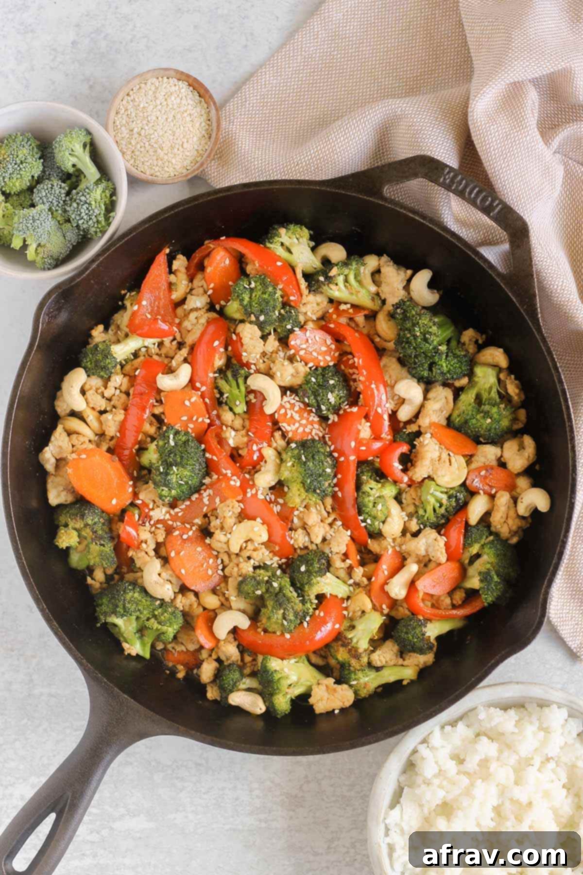 Ground chicken and veggie stir fry in a cast iron skillet with a bowl of broccoli and cooked rice on the side.