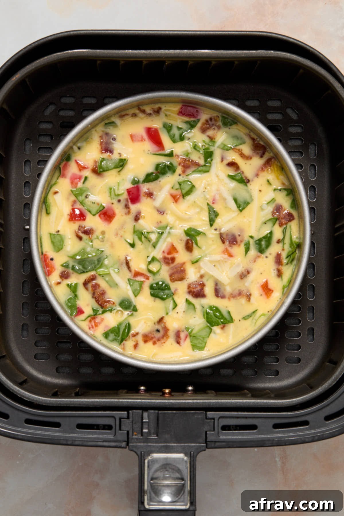 Velvety Air Fryer Frittata with Savory Spinach Bacon and Cheese 8 Uncooked frittata in a round pan placed in the air fryer basket, ready to cook.