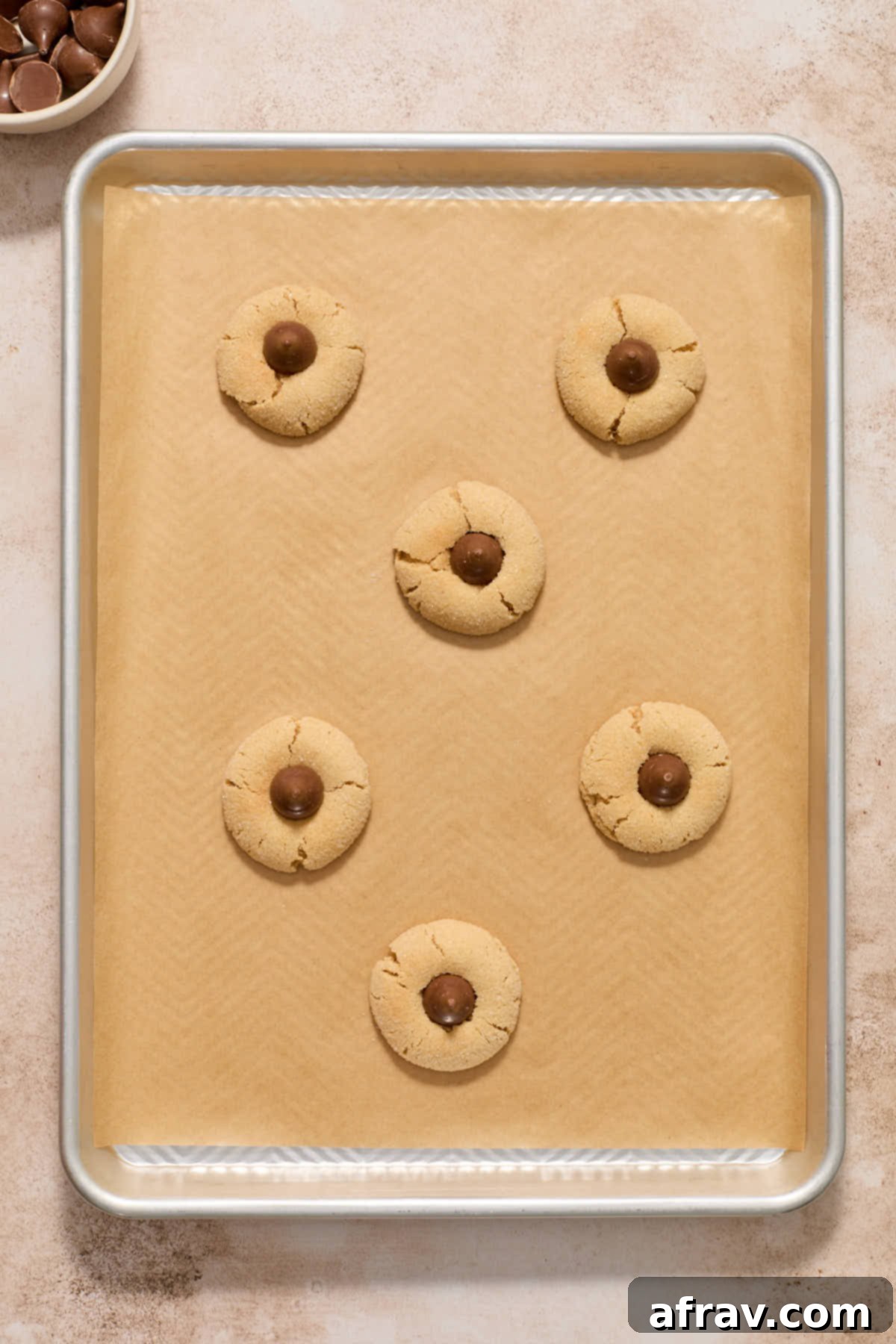 Warm peanut butter blossom cookies on a baking sheet, each with a chocolate kiss gently pressed into its center, creating the iconic blossom shape.
