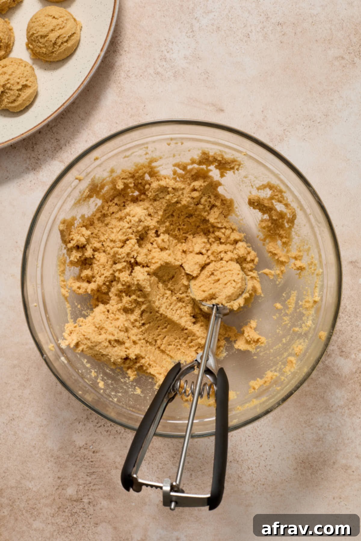 Using a cookie scoop, portions of almond flour peanut butter cookie dough are neatly arranged on a plate, ready for chilling.