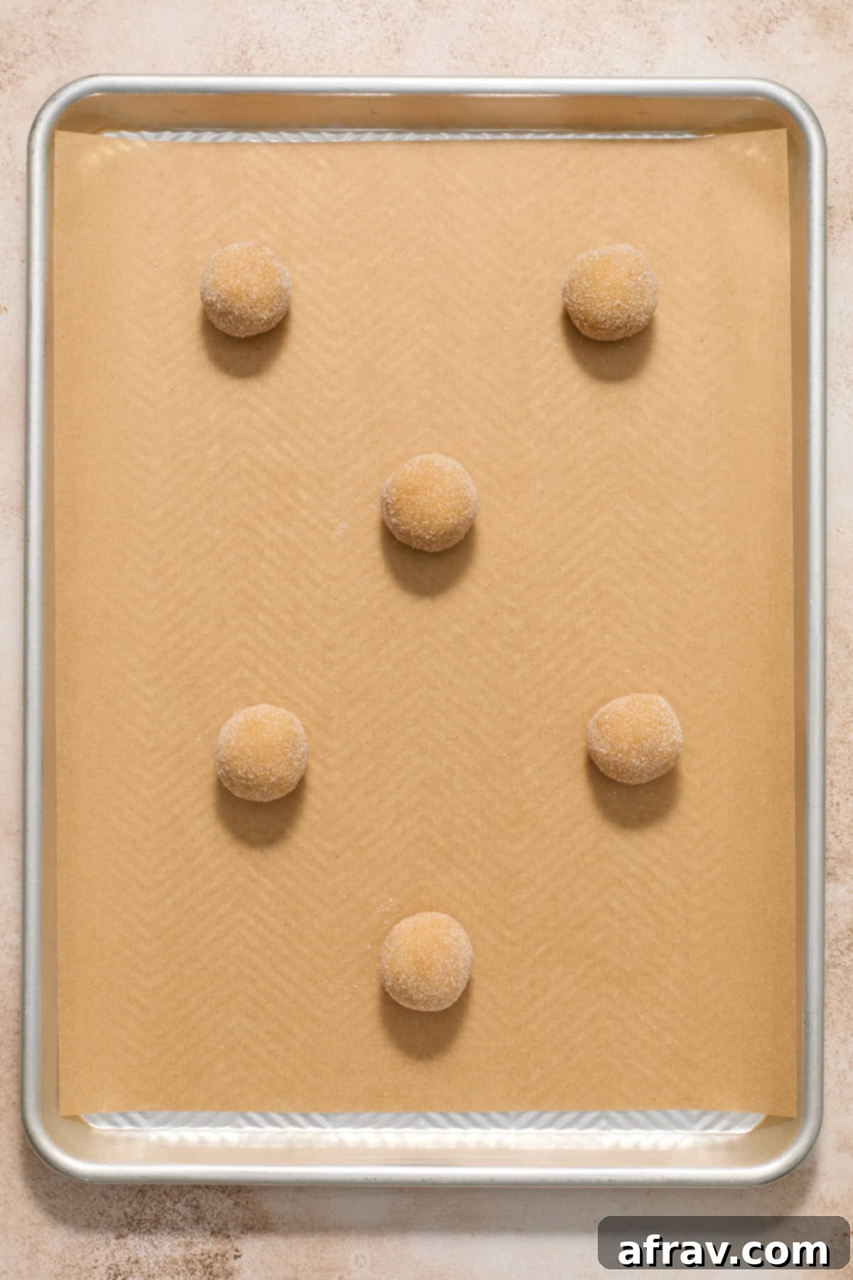 Neatly arranged sugar-coated almond flour peanut butter cookie dough balls on a parchment paper-lined baking sheet, spaced perfectly for baking.