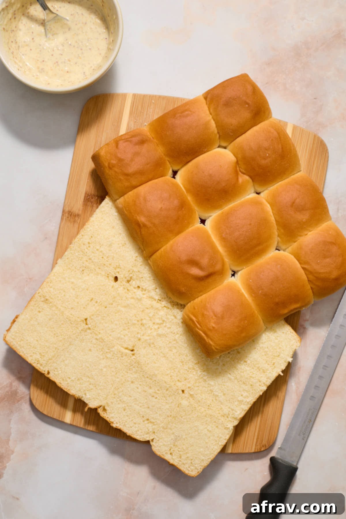 Sweet rolls cut in half horizontally on a wooden board with mayo/mustard mixture on the side.